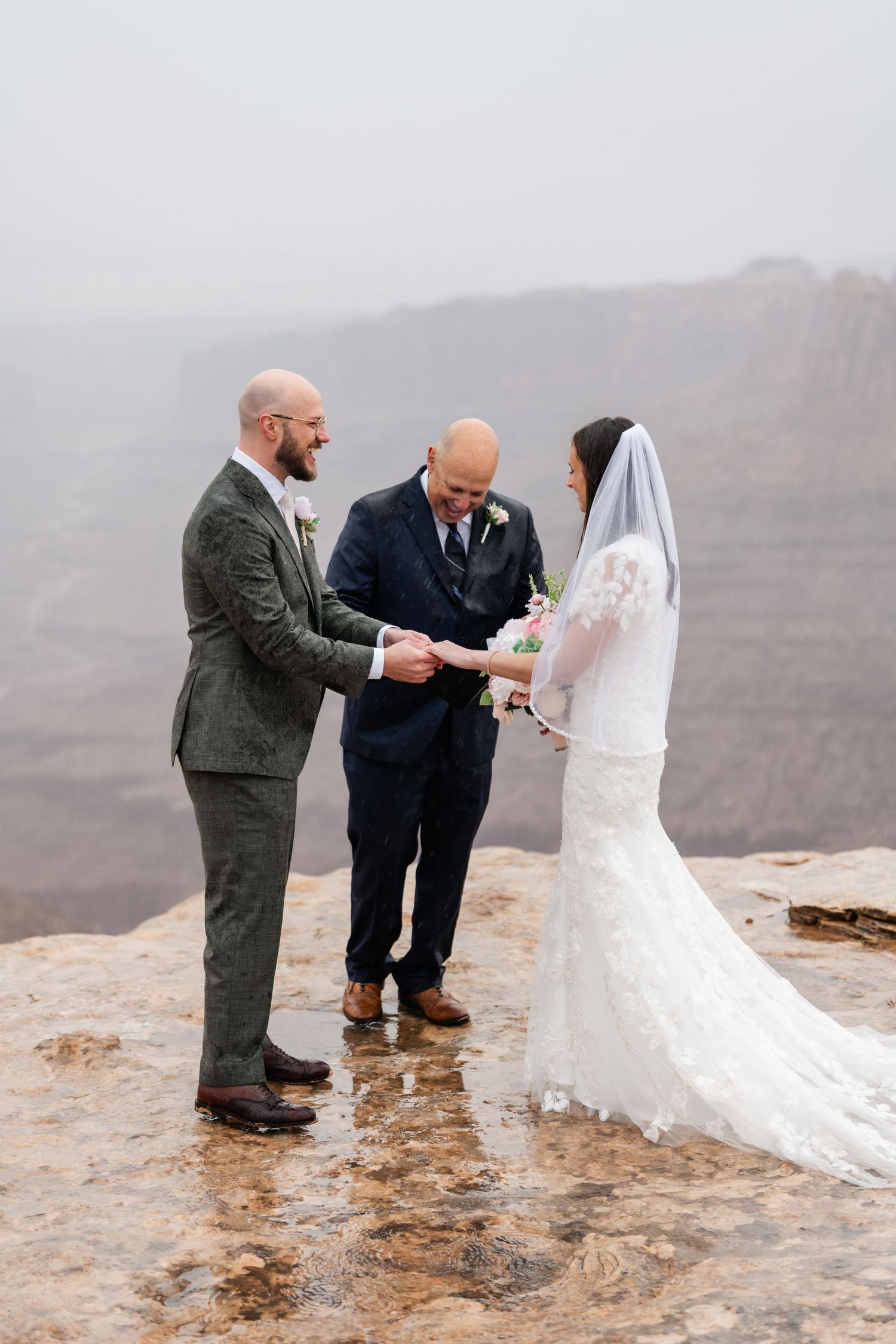 Small wedding party gathered on desert cliff edge for intimate ceremony in misty conditions.