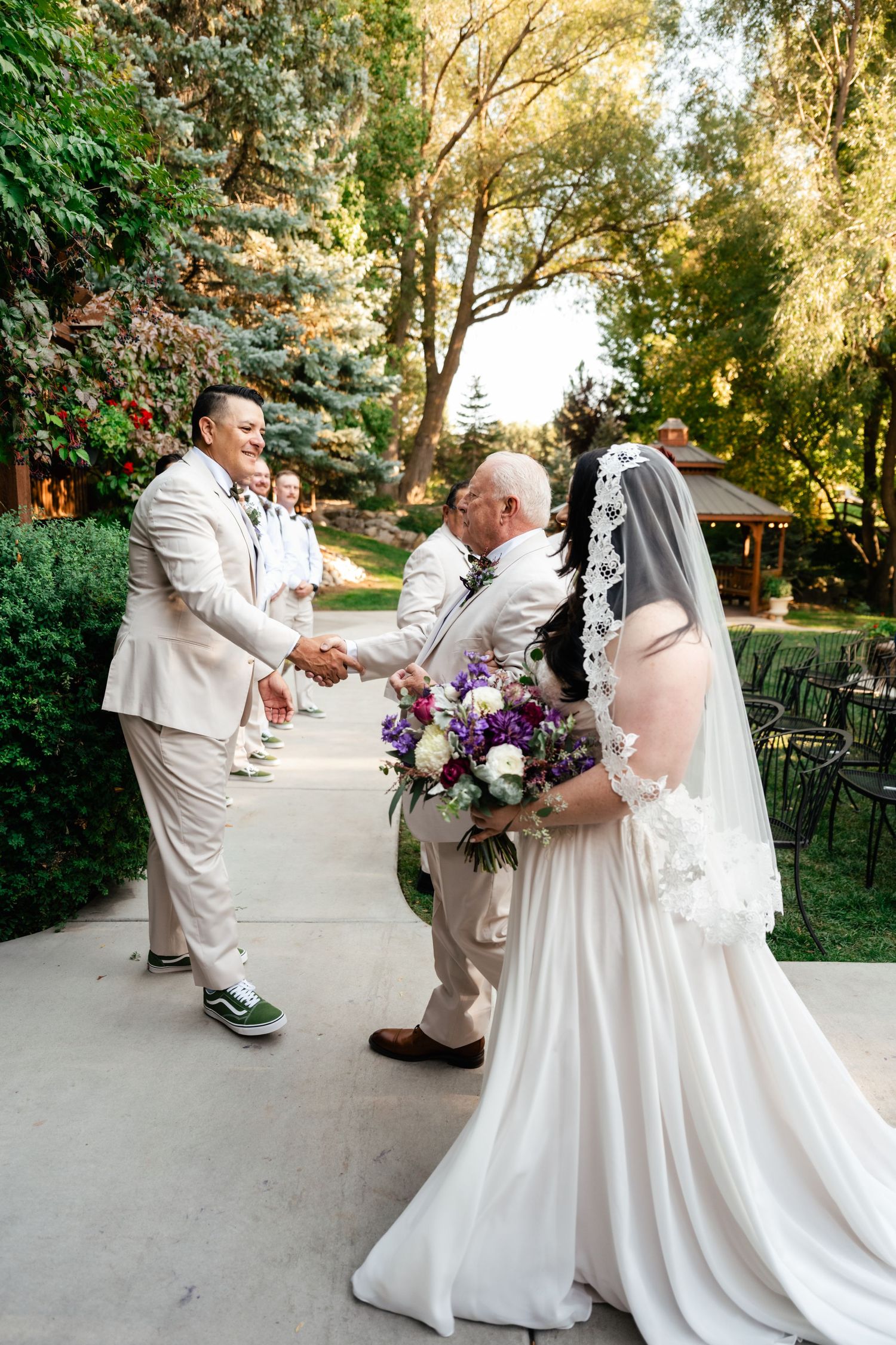 Wedding ceremony moment on outdoor garden path with wedding party in light colored attire.