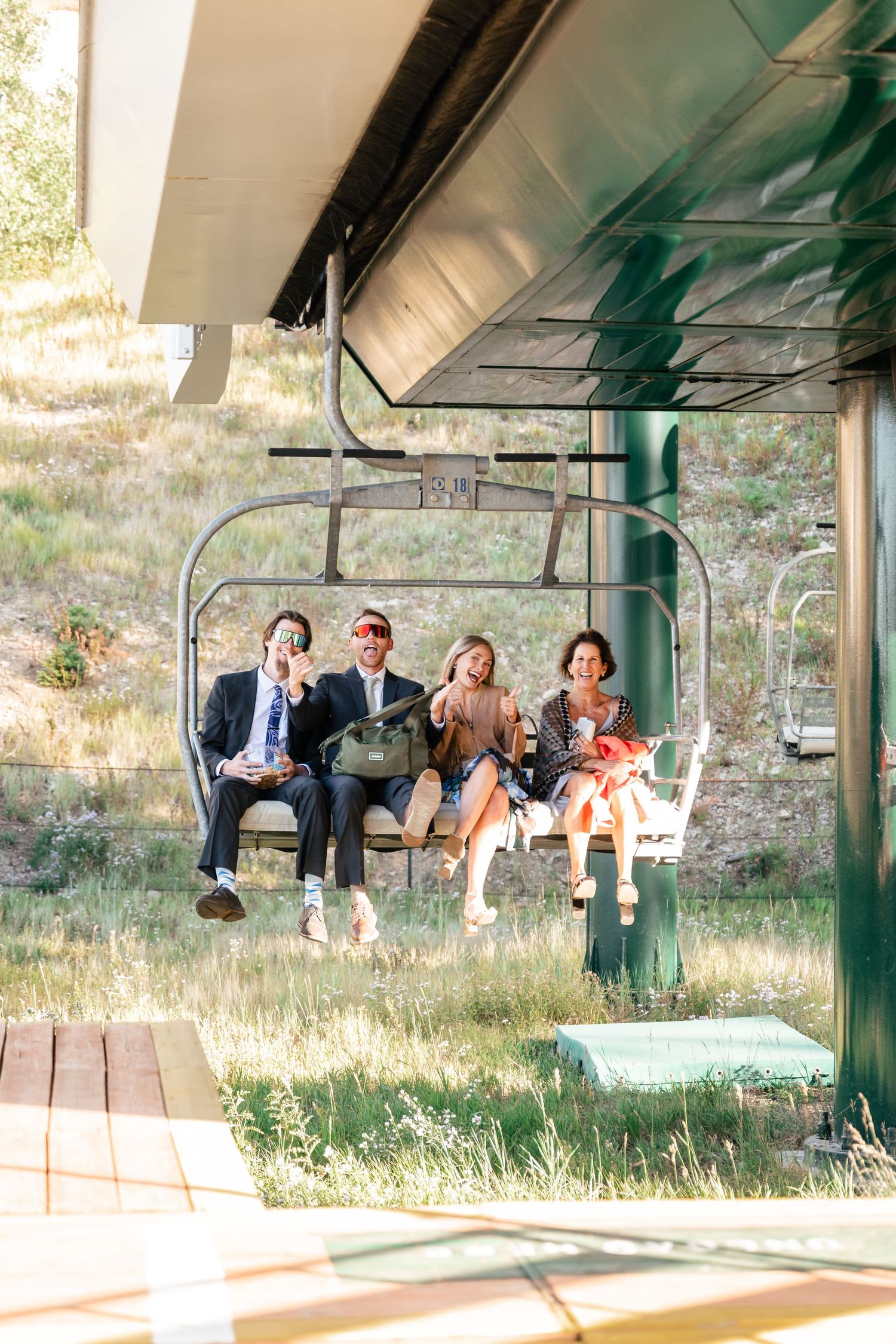 Wedding party sits together on a ski lift chair during summer mountain wedding. Park City Wedding Photographer. Utah Wedding Photographer.