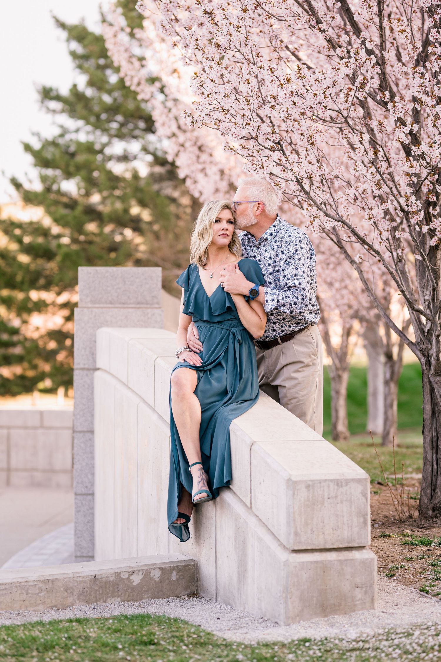 A couple shares an intimate moment on stone steps surrounded by blooming cherry trees.