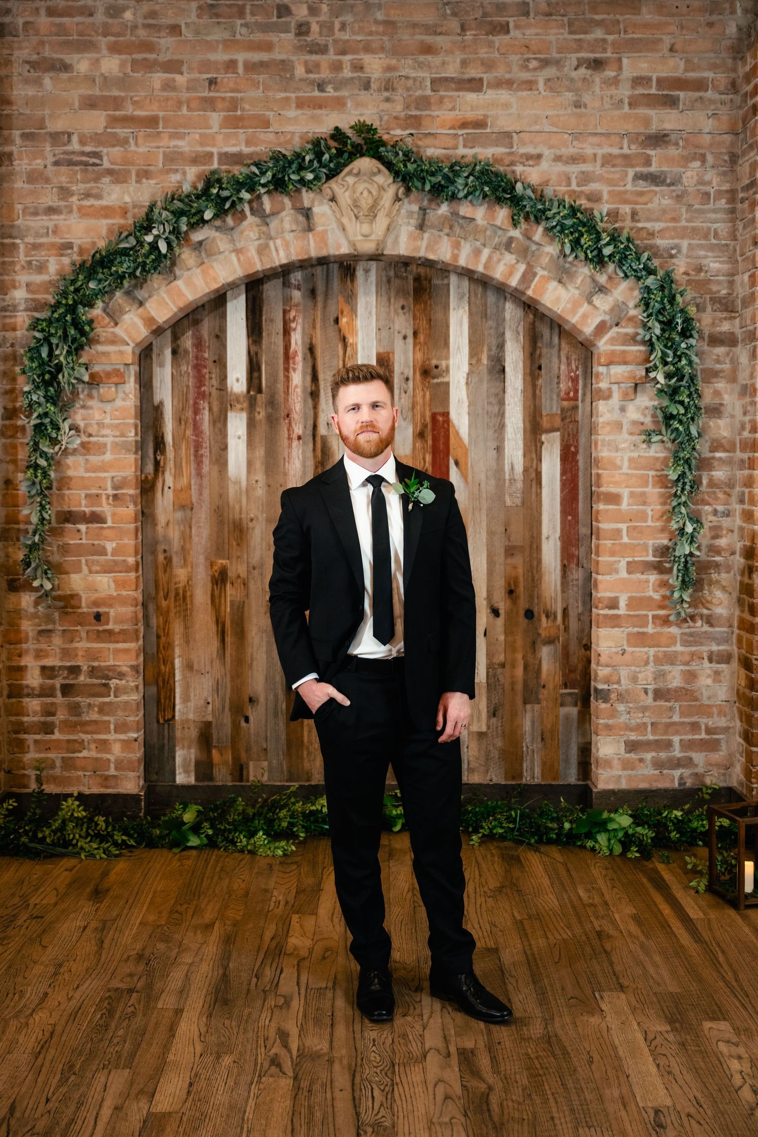 A formal event setup with an elegant wooden door arch decorated with greenery against exposed brick walls.