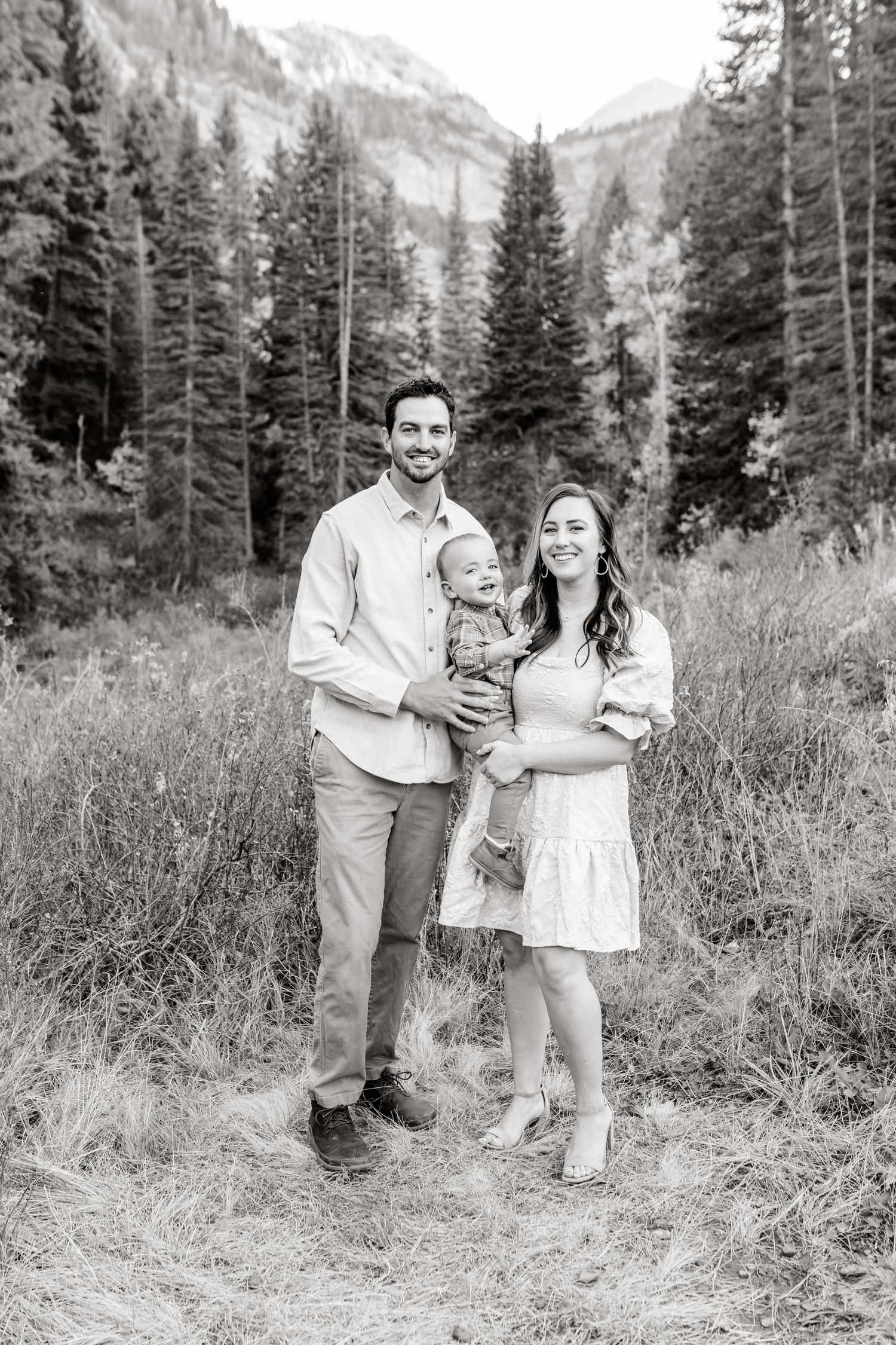 Black and white family portrait in mountain setting with evergreen trees.