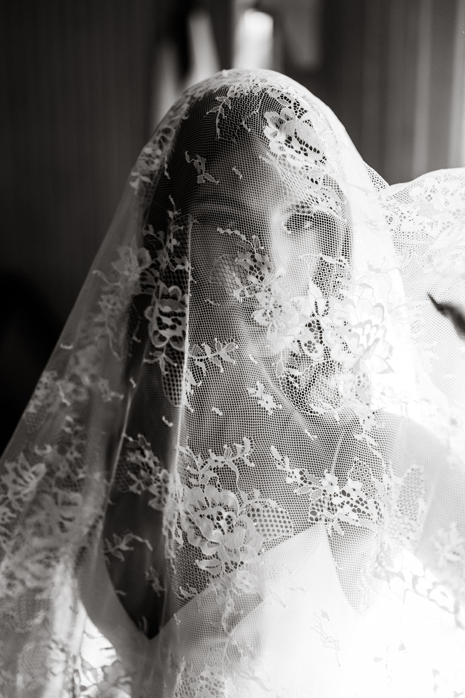 Black and white portrait of a bride with lace veil draped over her face showing floral details.