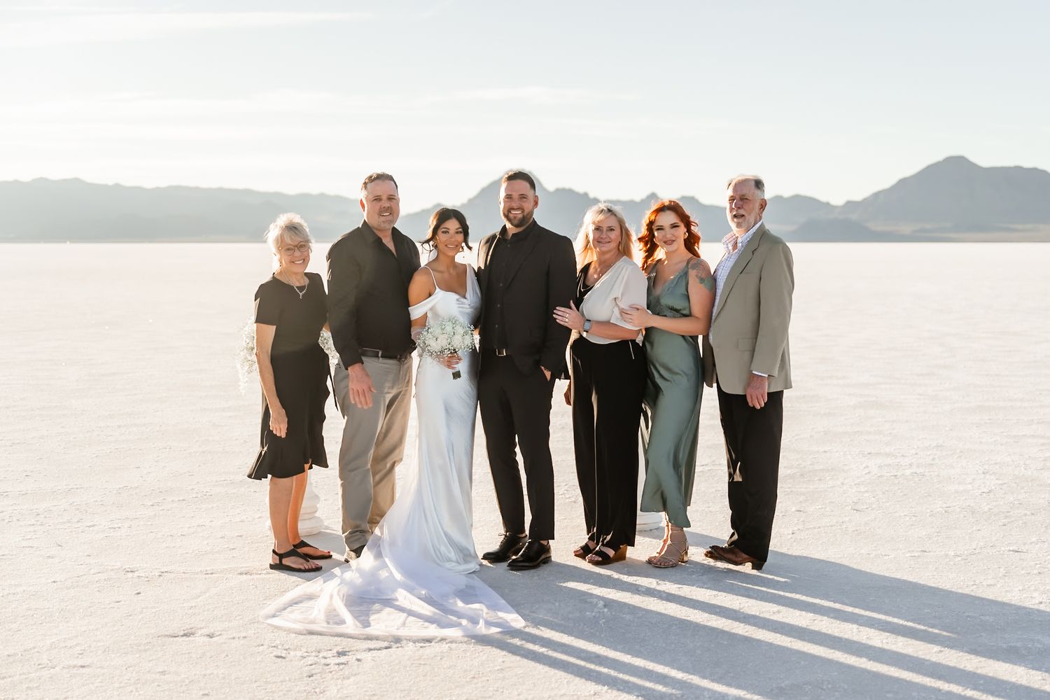 Wedding party standing together on salt flats creating long shadows at sunset.