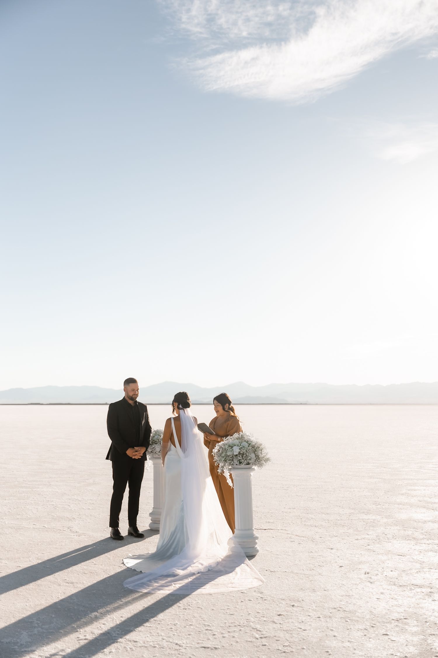 Wedding ceremony setup on salt flats with white columns and dramatic mountain backdrop.
