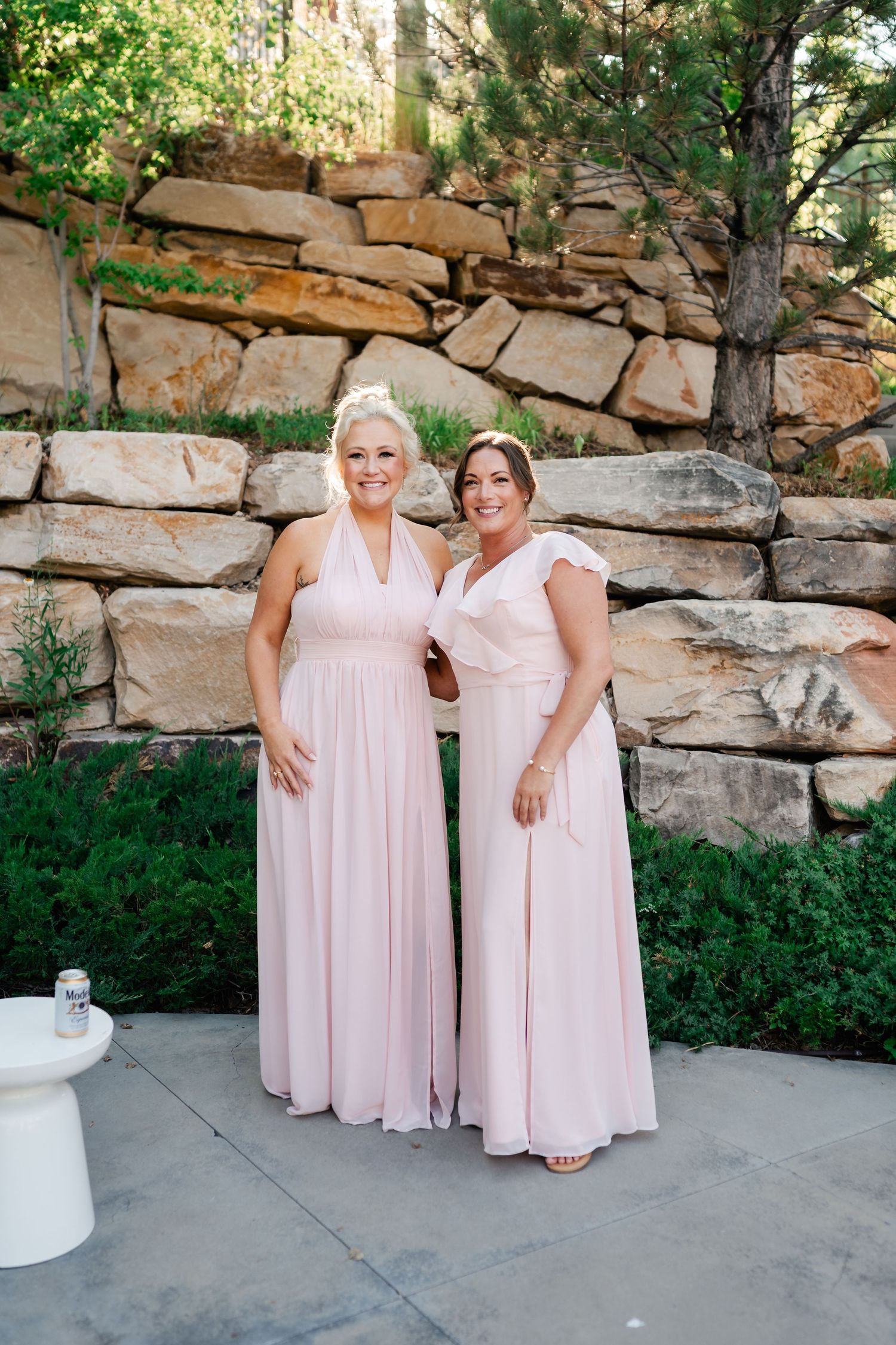 People in soft pink dresses pose together against a natural stone wall backdrop.