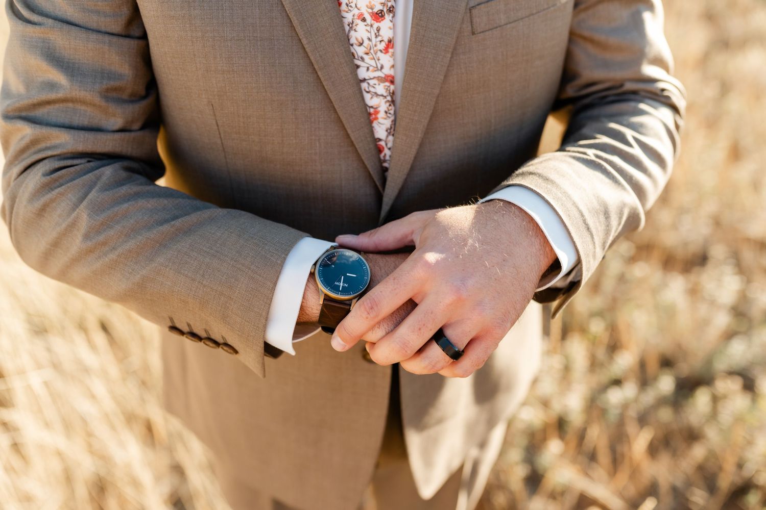 Professional wearing a tan suit checks their modern smartwatch against a blurred outdoor background.