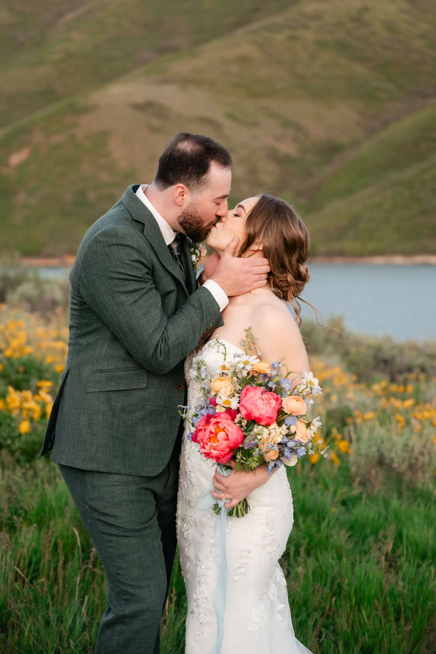 A couple shares intimate kisses during their mountain wedding photoshoot with colorful bouquet.