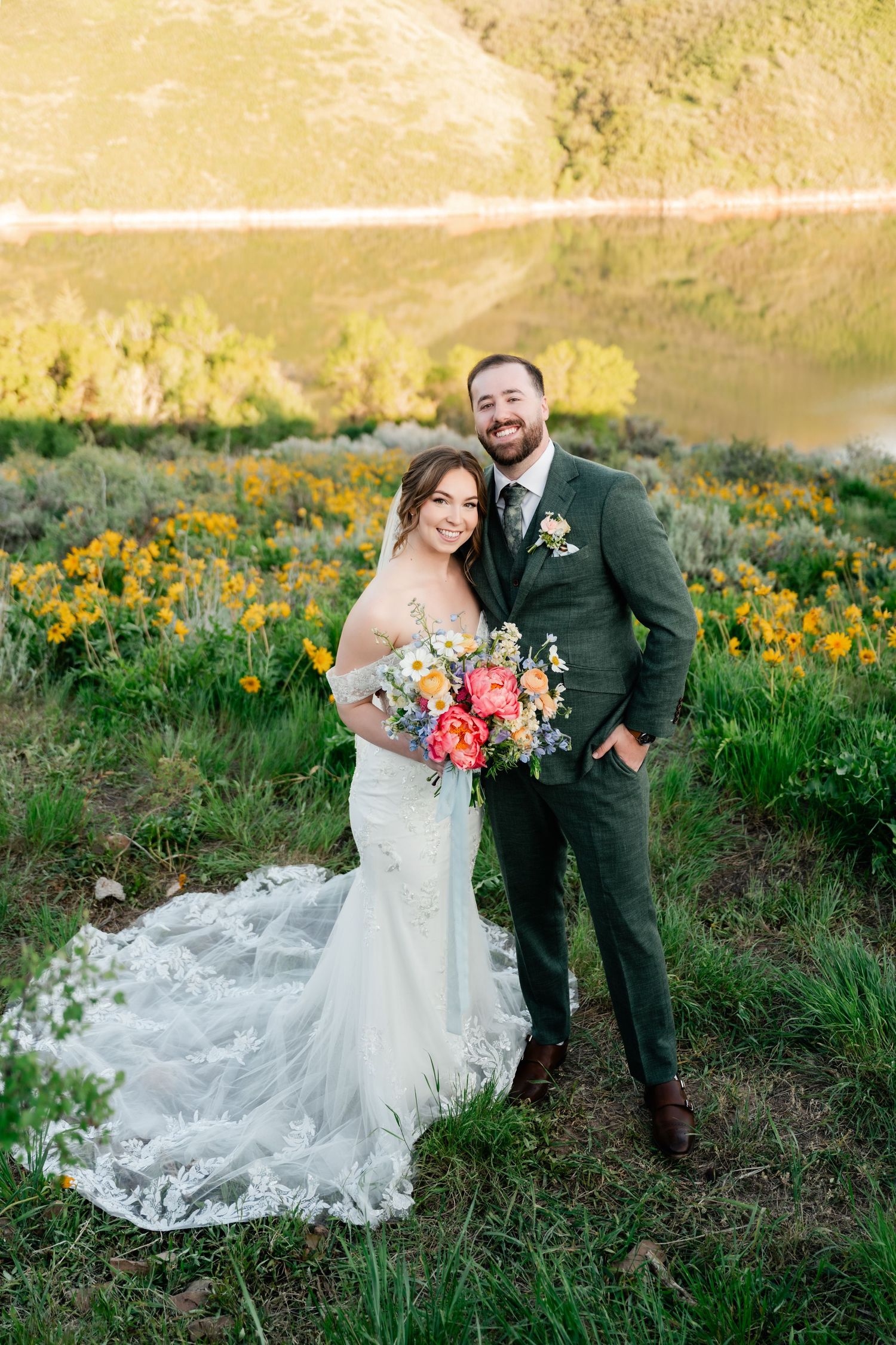 Newlyweds share intimate moment in mountain field with colorful bouquet and flowing wedding dress.