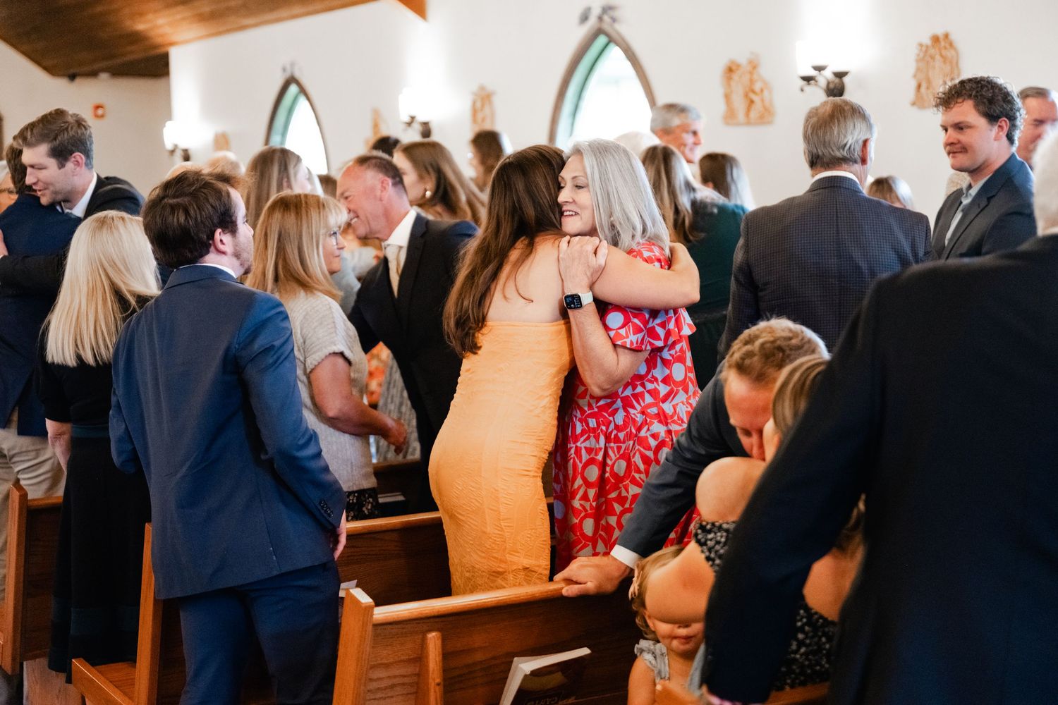 Side view of wedding guests seated in wooden church pews during ceremony.