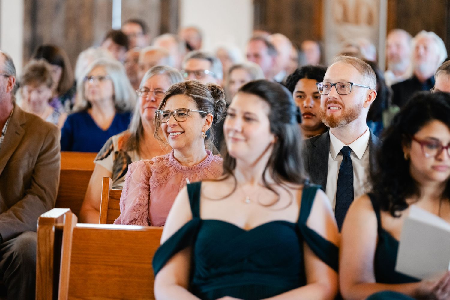 Wedding guests share joyful moments while seated in church pews during the ceremony.