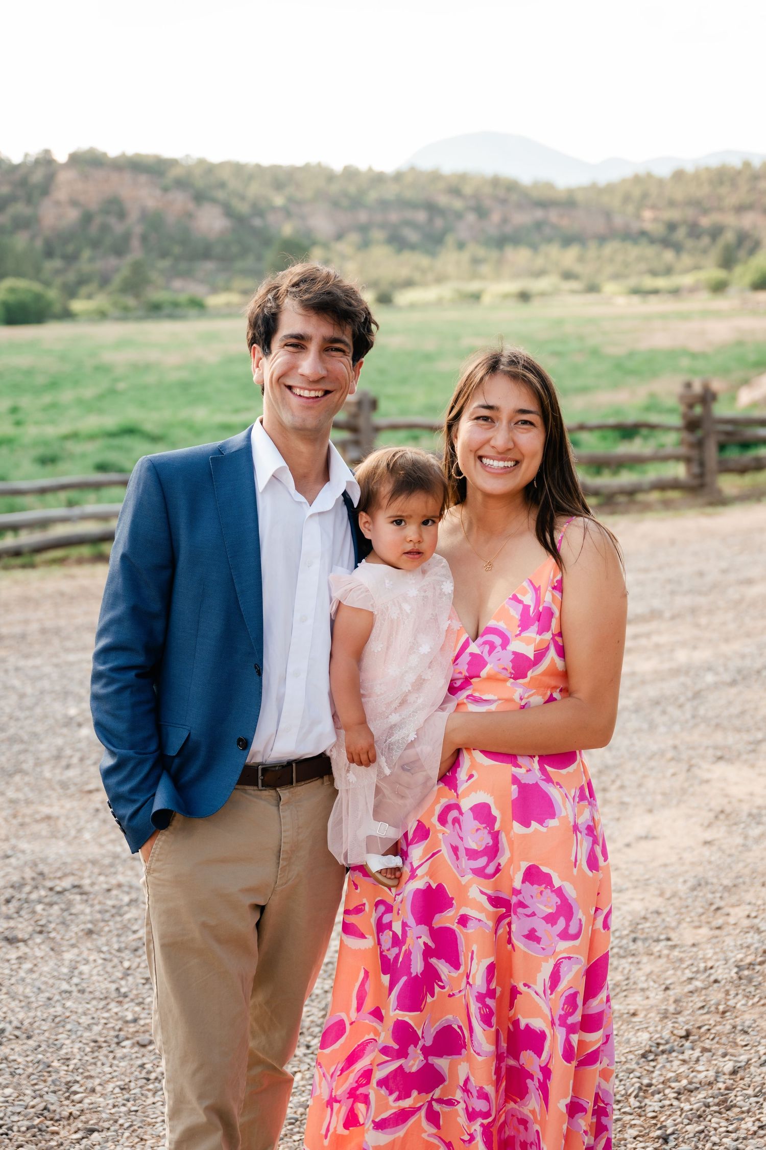 Family poses together in a casual outdoor setting with rolling hills in the background.