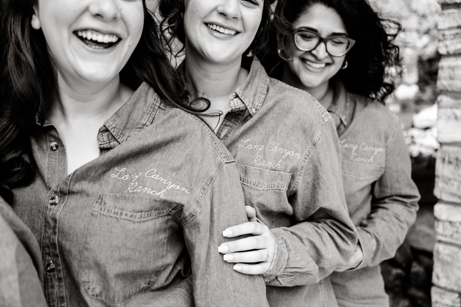 A group wearing coordinated denim and pink outfits smiles together against a stone wall backdrop.