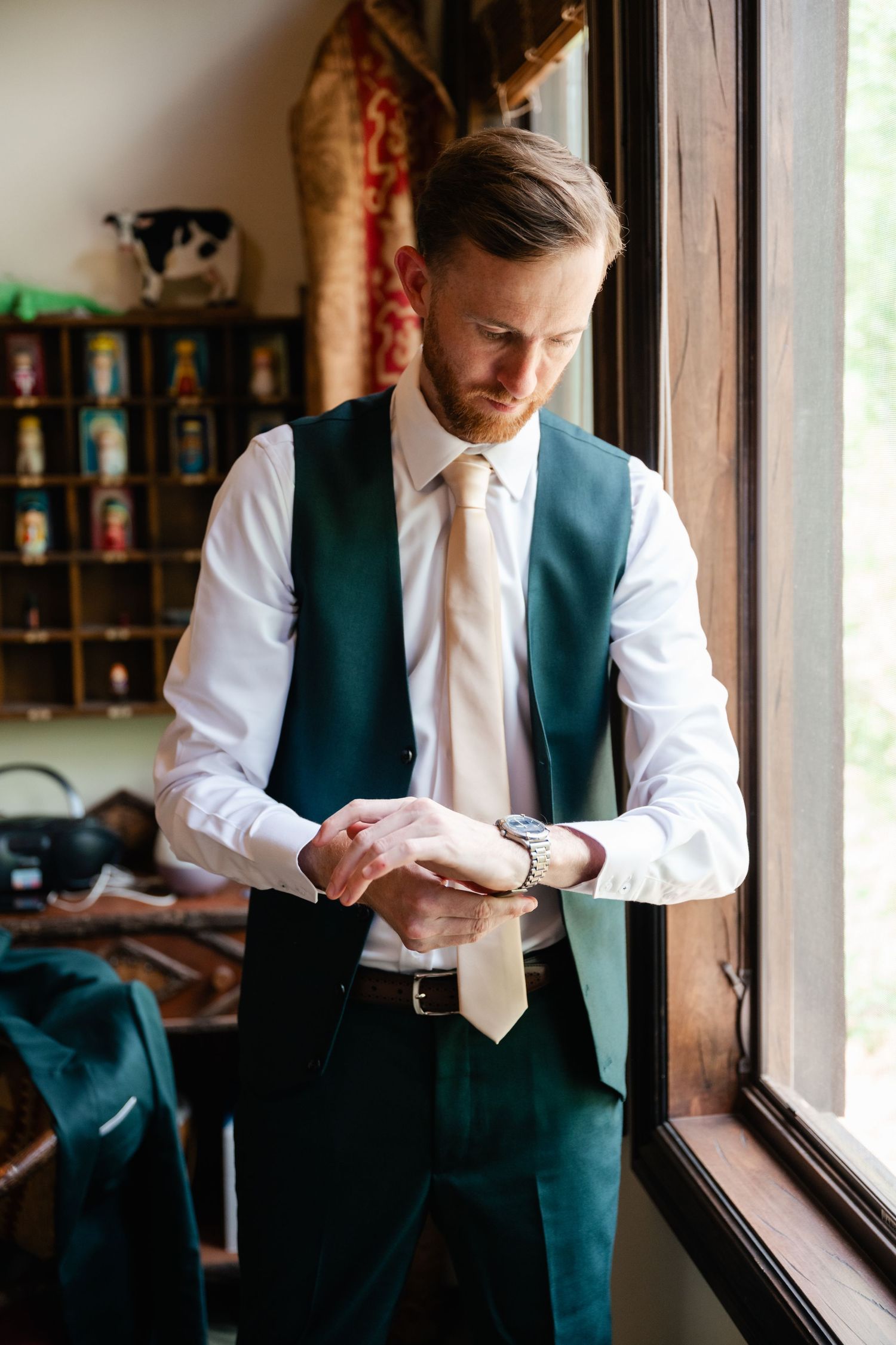 Person in formal attire adjusting their tie while standing by a window.