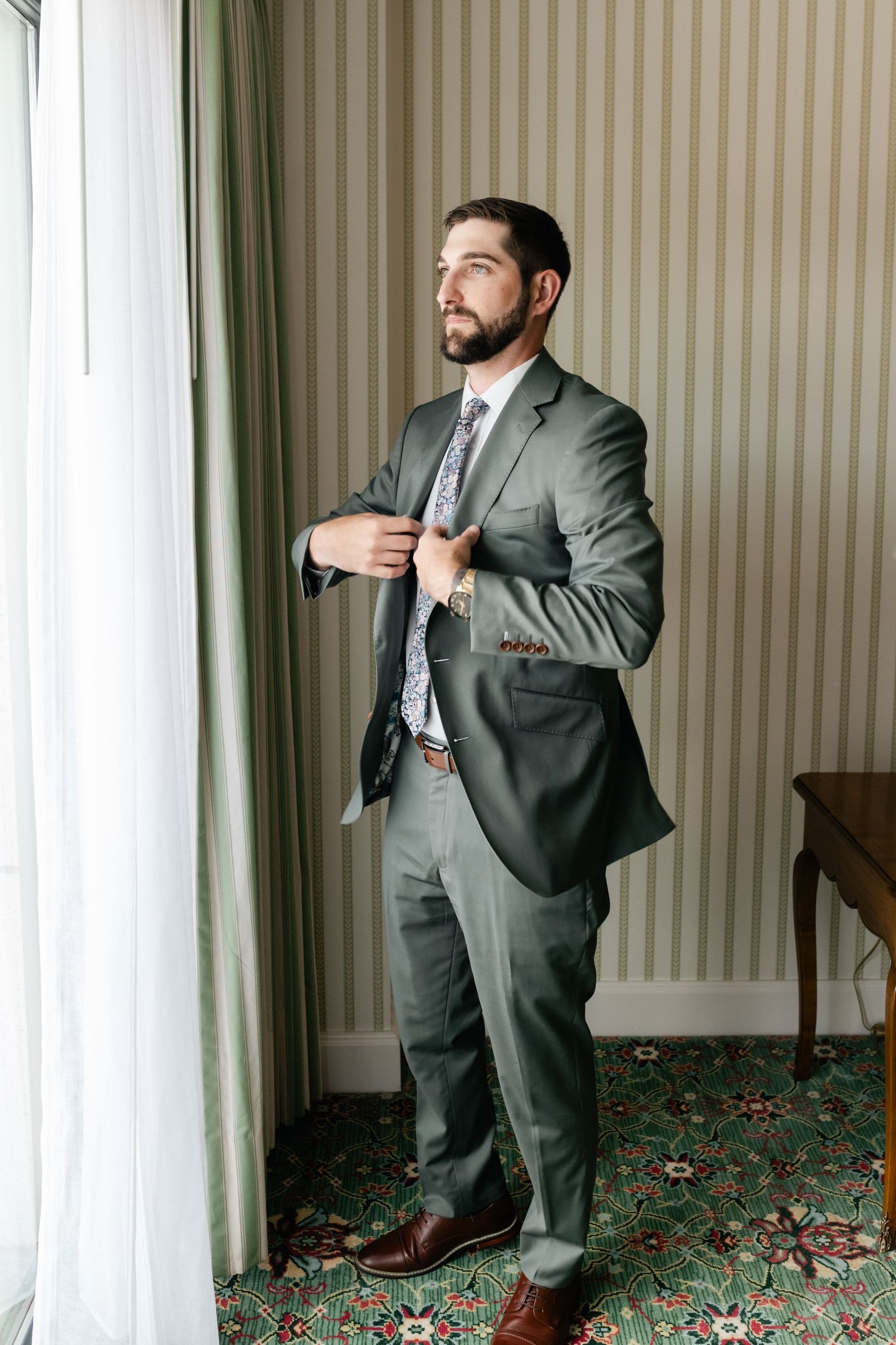 Series of photos showing a person in a grey suit adjusting their tie against a striped wallpaper background.