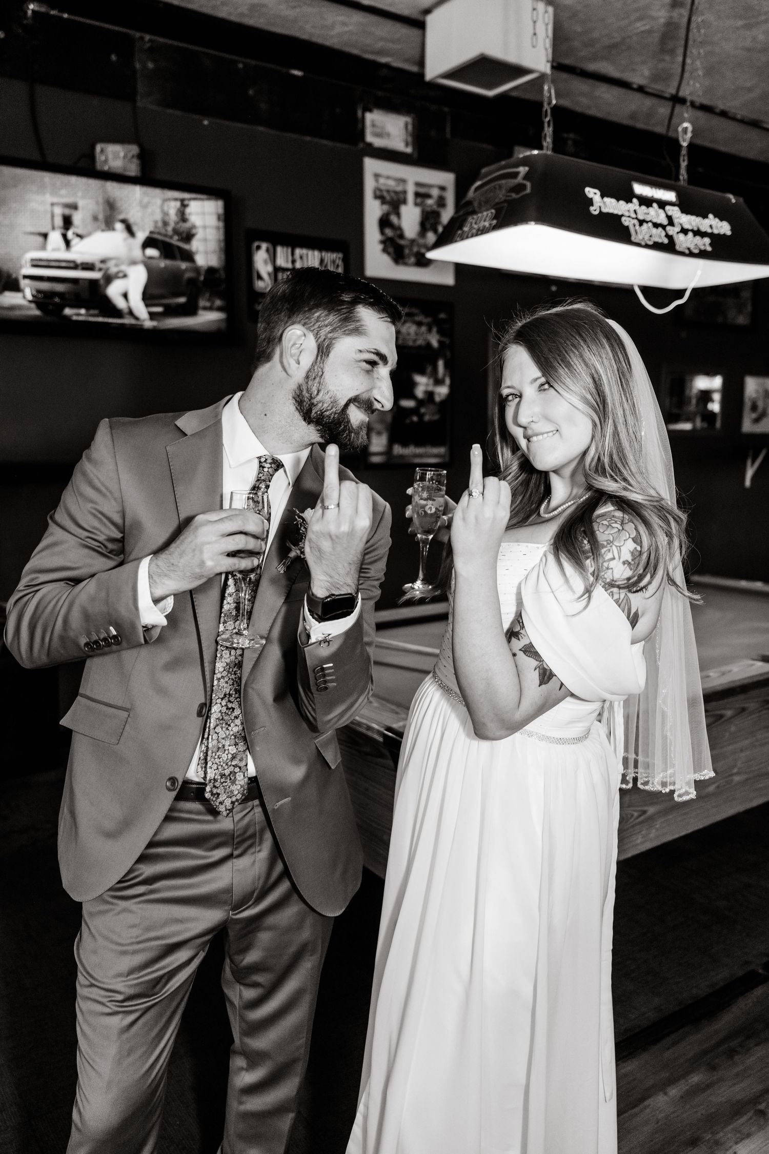 A couple shares drinks and laughs at a bar in formal attire during a celebration.