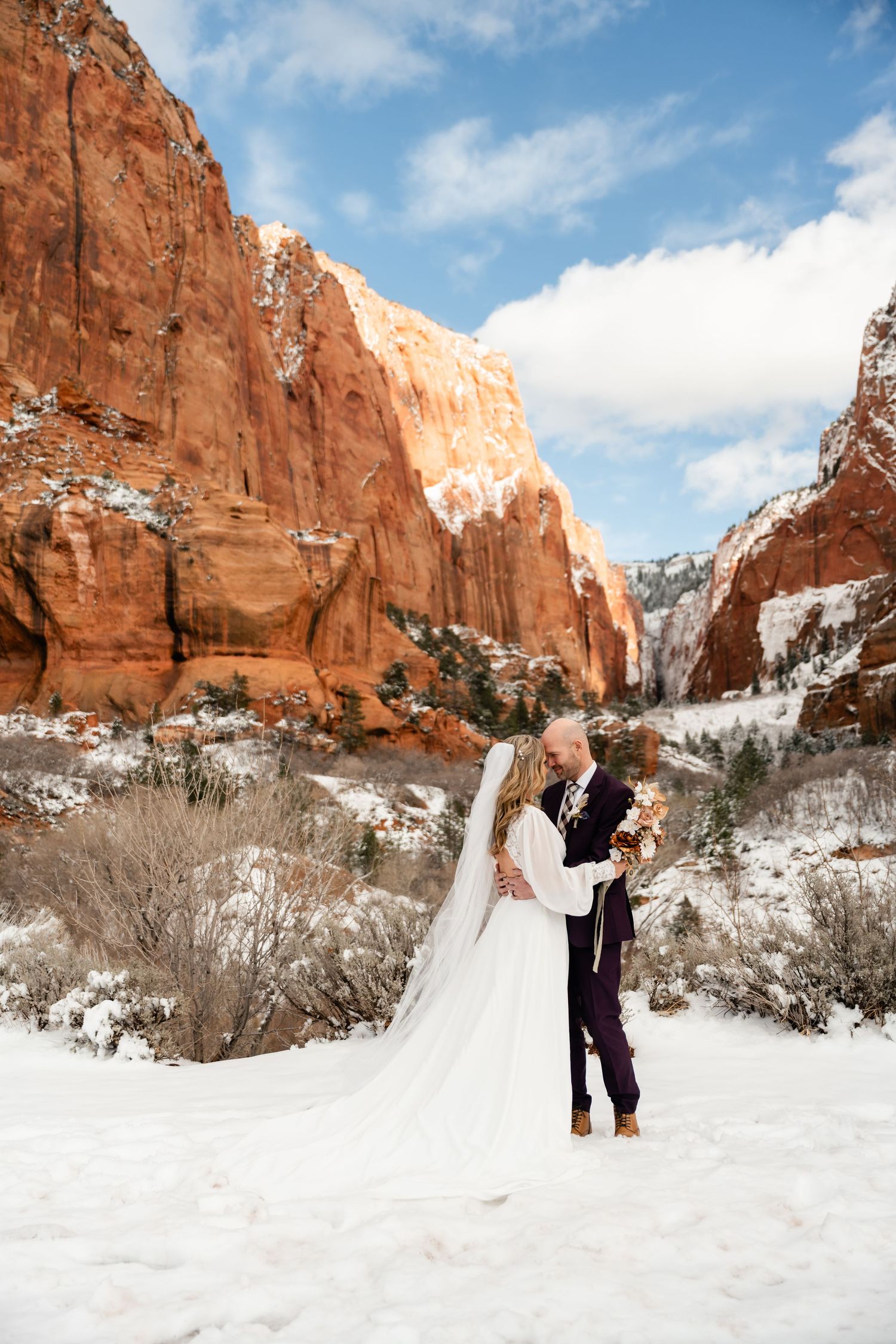 A couple celebrates their wedding day in a snowy landscape with towering red rock formations.