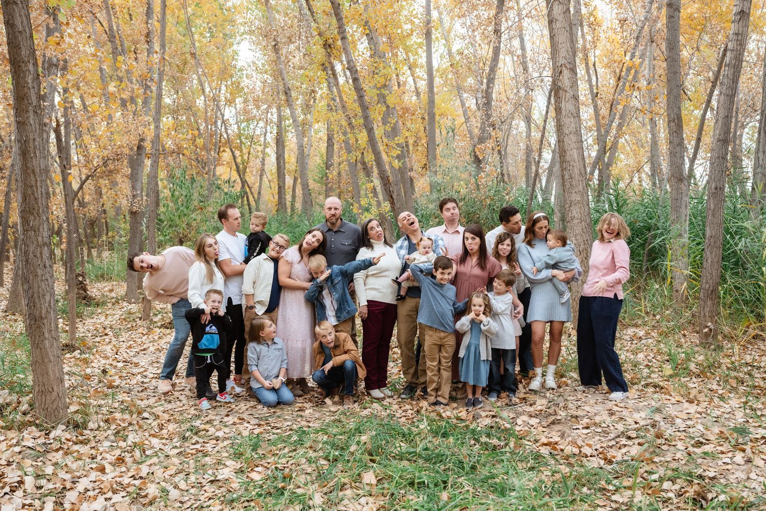 Large group gathered in autumn forest with golden leaves and tall trees for outdoor photography session.