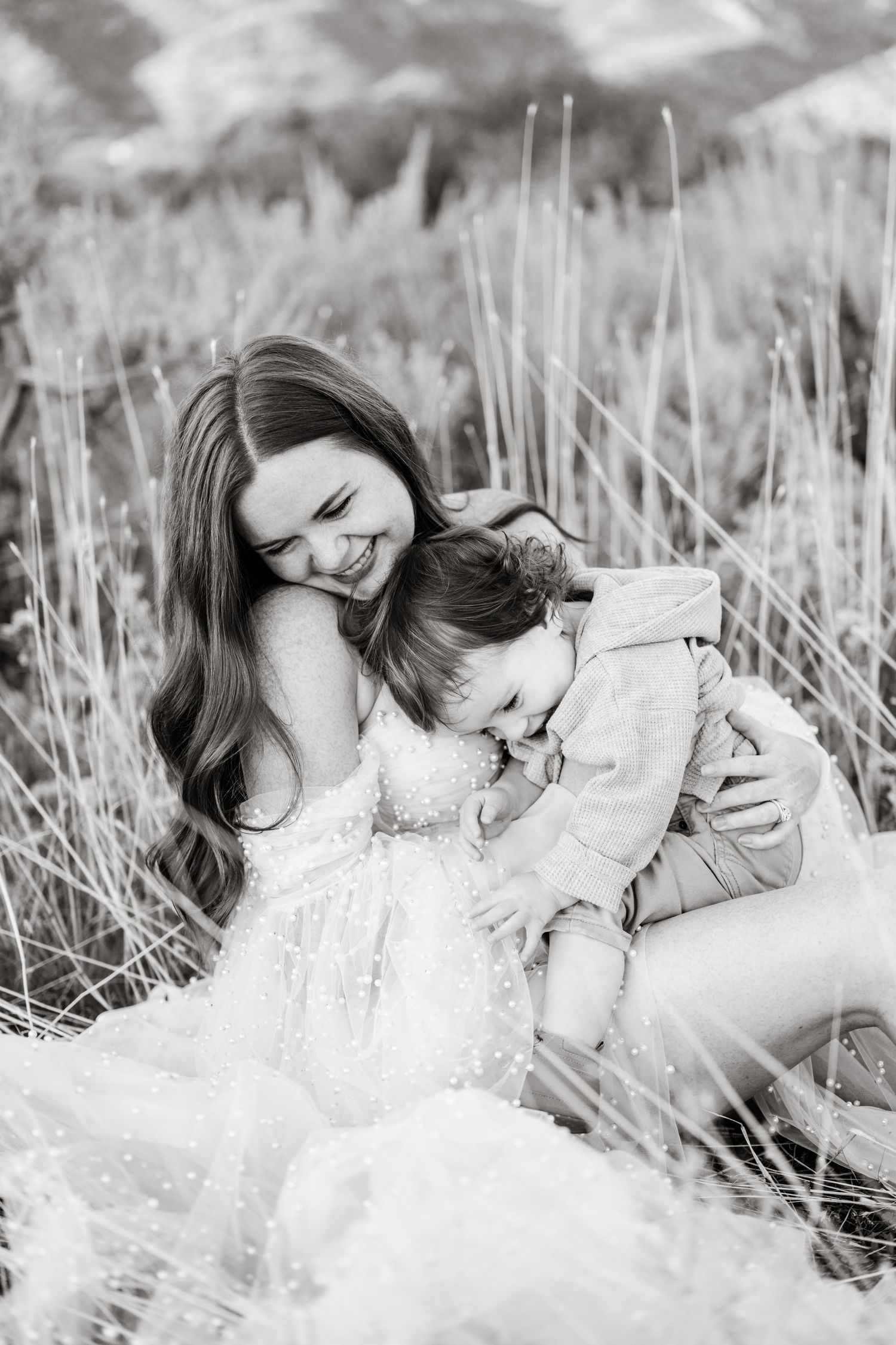 Black and white maternity photos captured in tall grass with a delicate lace dress.