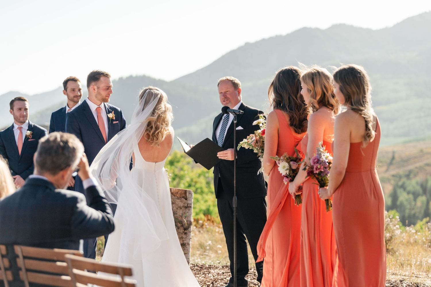 A wedding ceremony takes place on a mountain overlook with bridesmaids in coral dresses and scenic backdrop. Park City Wedding Photographer