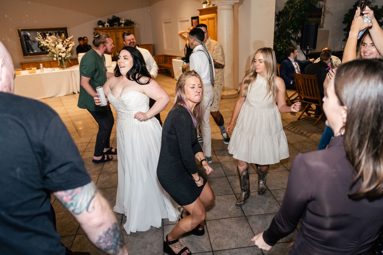Wedding reception guests dance and celebrate together on the dance floor at an indoor venue.
