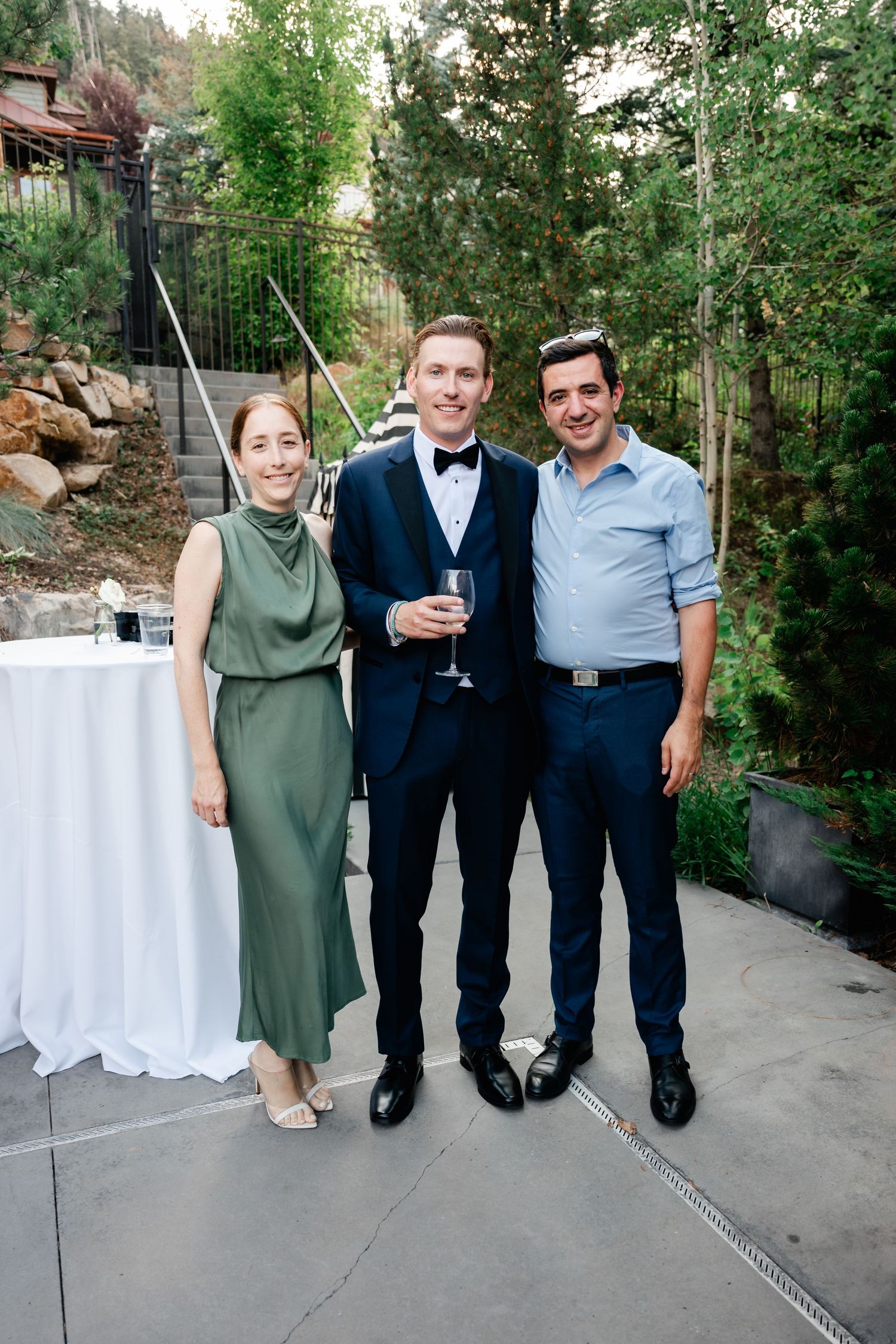 Three guests posing at elegant wedding cocktail hour in lush garden setting by the pool outside the Washington School House Hotel.
