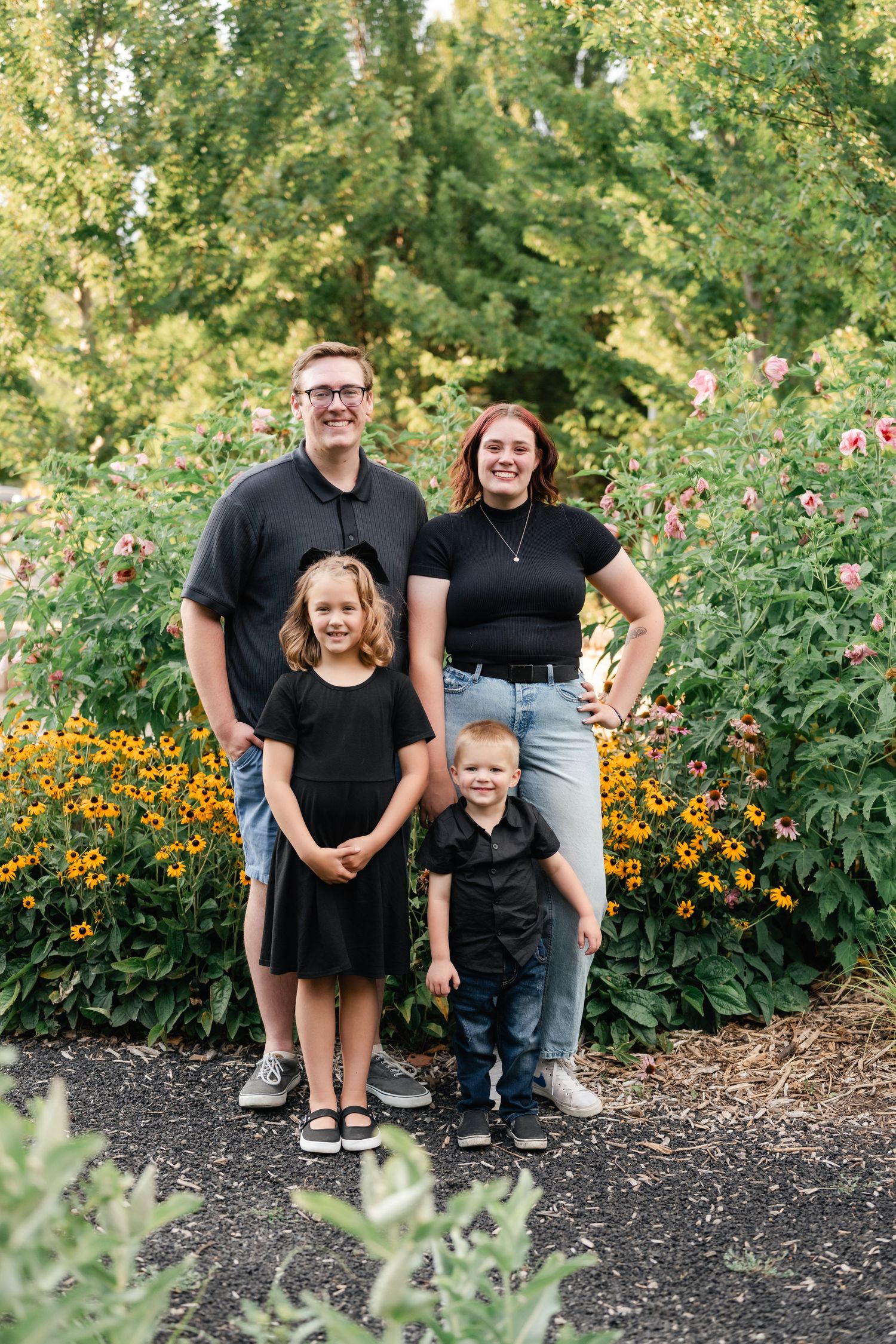 A family poses together in front of a vibrant garden with yellow and orange flowers blooming in the background.