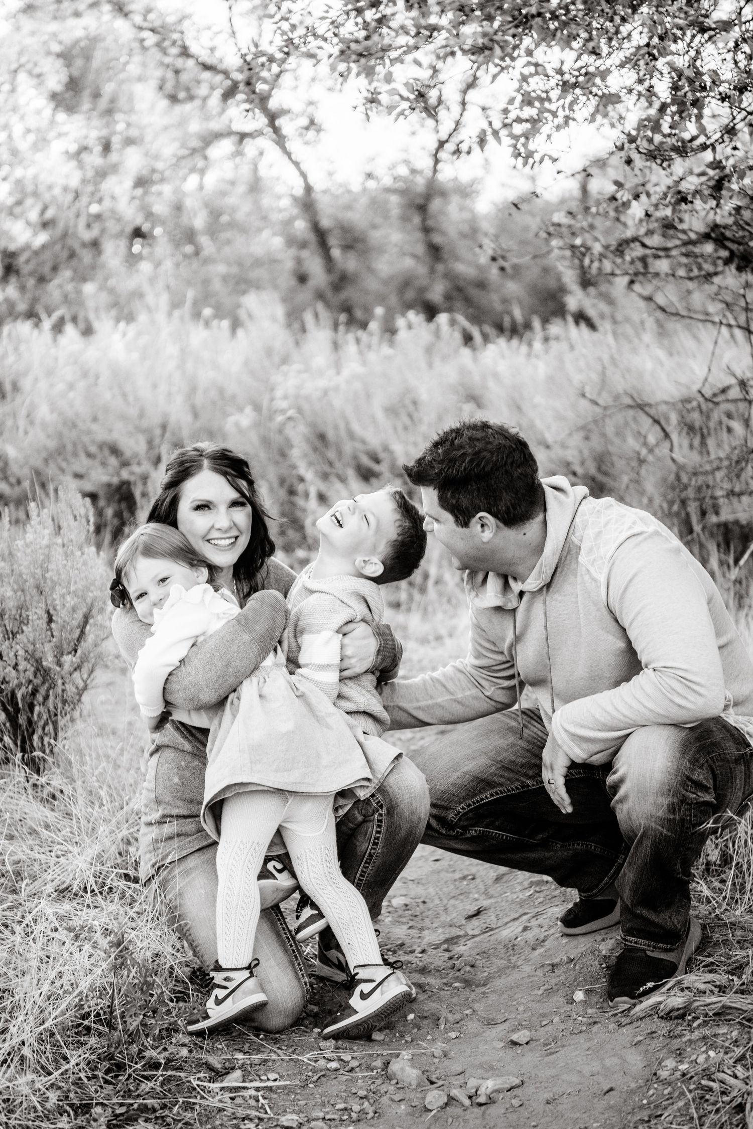 A couple sits together on the ground sharing intimate black and white moments in a natural outdoor setting.