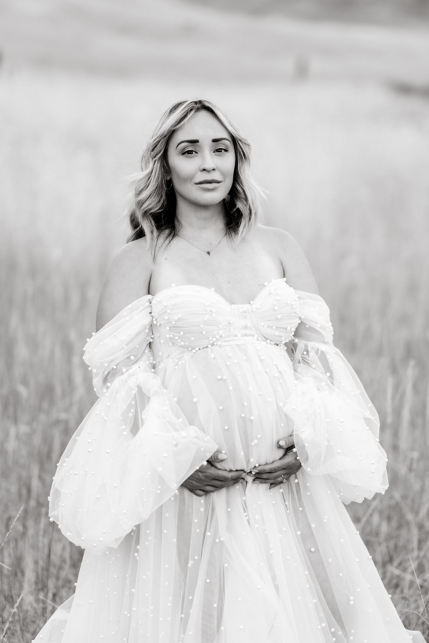 Romantic white lace dress billows softly in black and white portrait series among tall grasses.