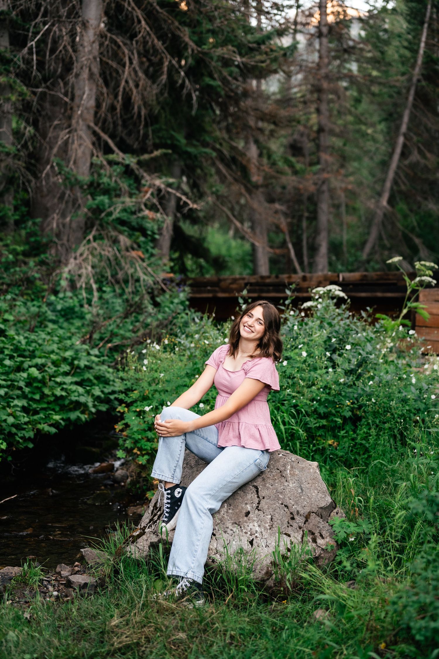 A figure sits on a large rock surrounded by lush greenery in a forest setting at sunset.