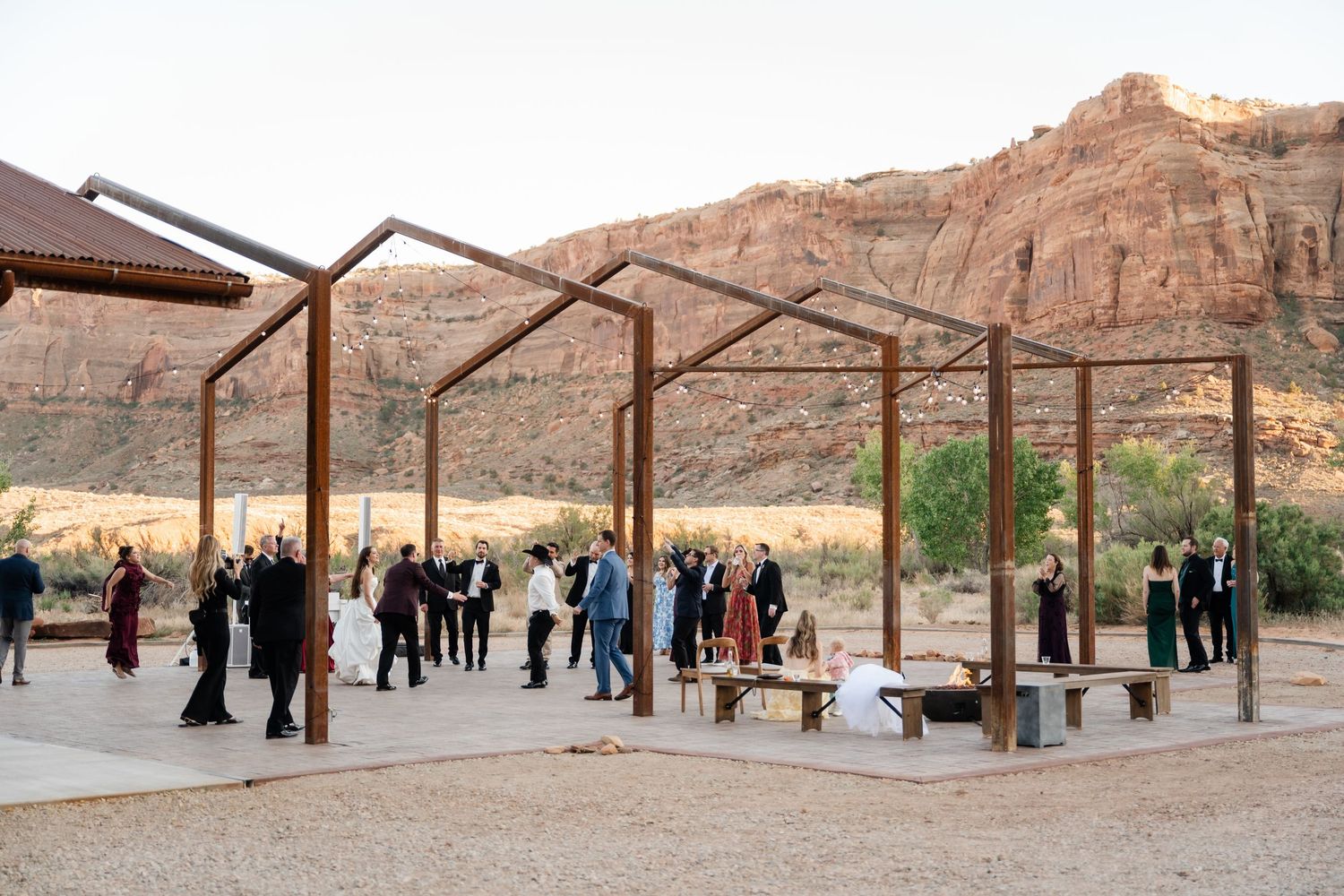 Outdoor wedding reception under rustic metal pergola with red rock canyon backdrop at dusk in desert landscape.