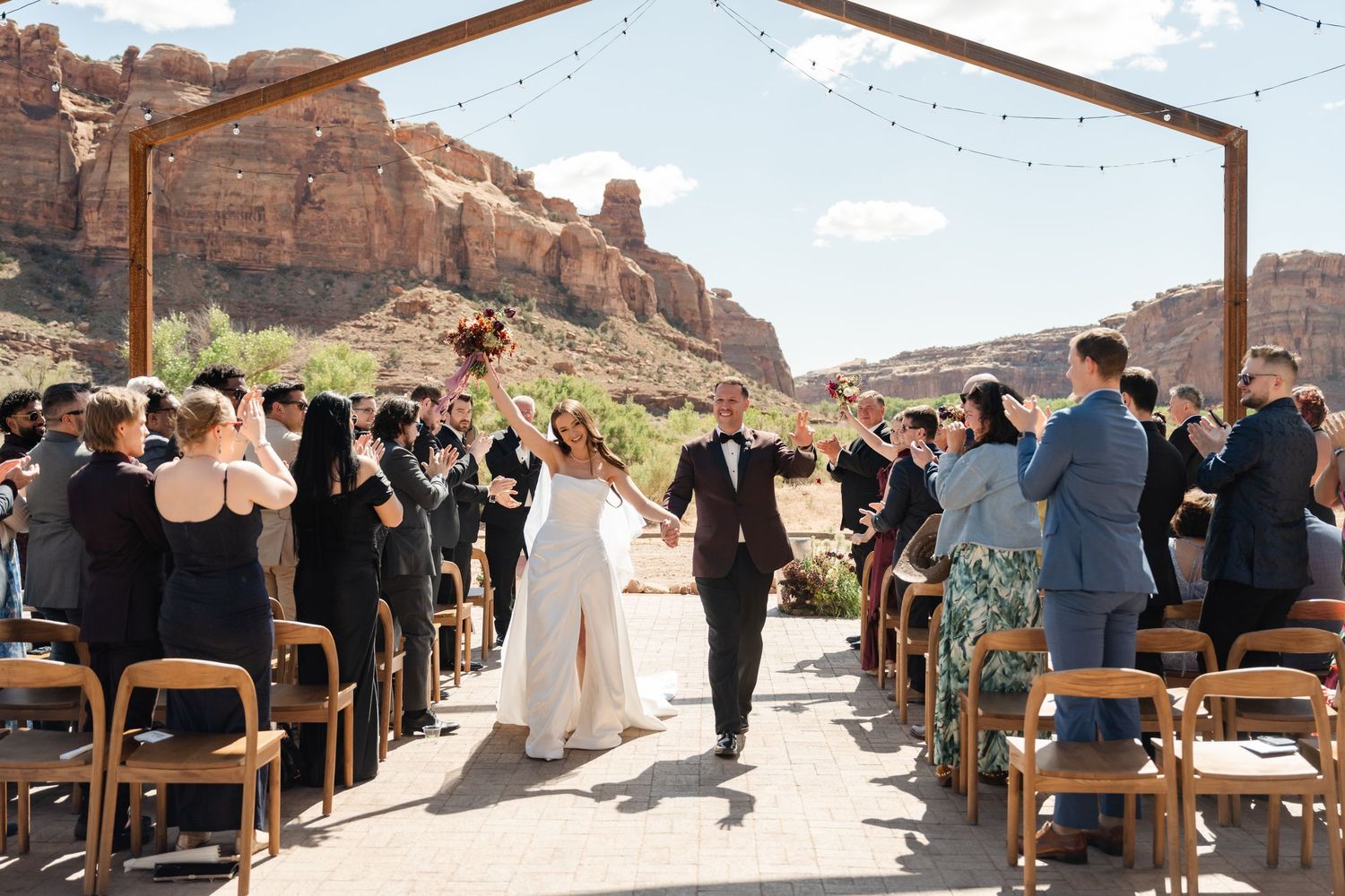 Bride and groom walk down the aisle at an outdoor desert wedding ceremony with red rock canyon backdrop.