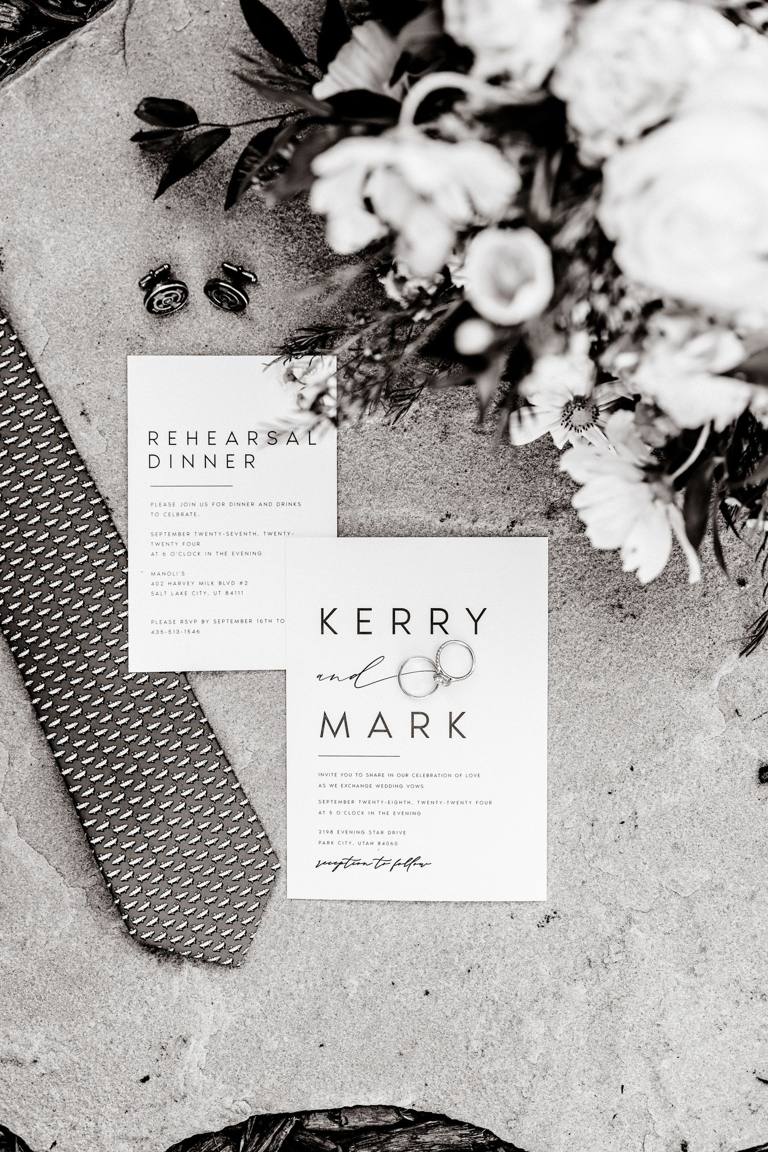 Elegant black and white wedding invitation with rehearsal dinner card and floral decor on concrete surface.