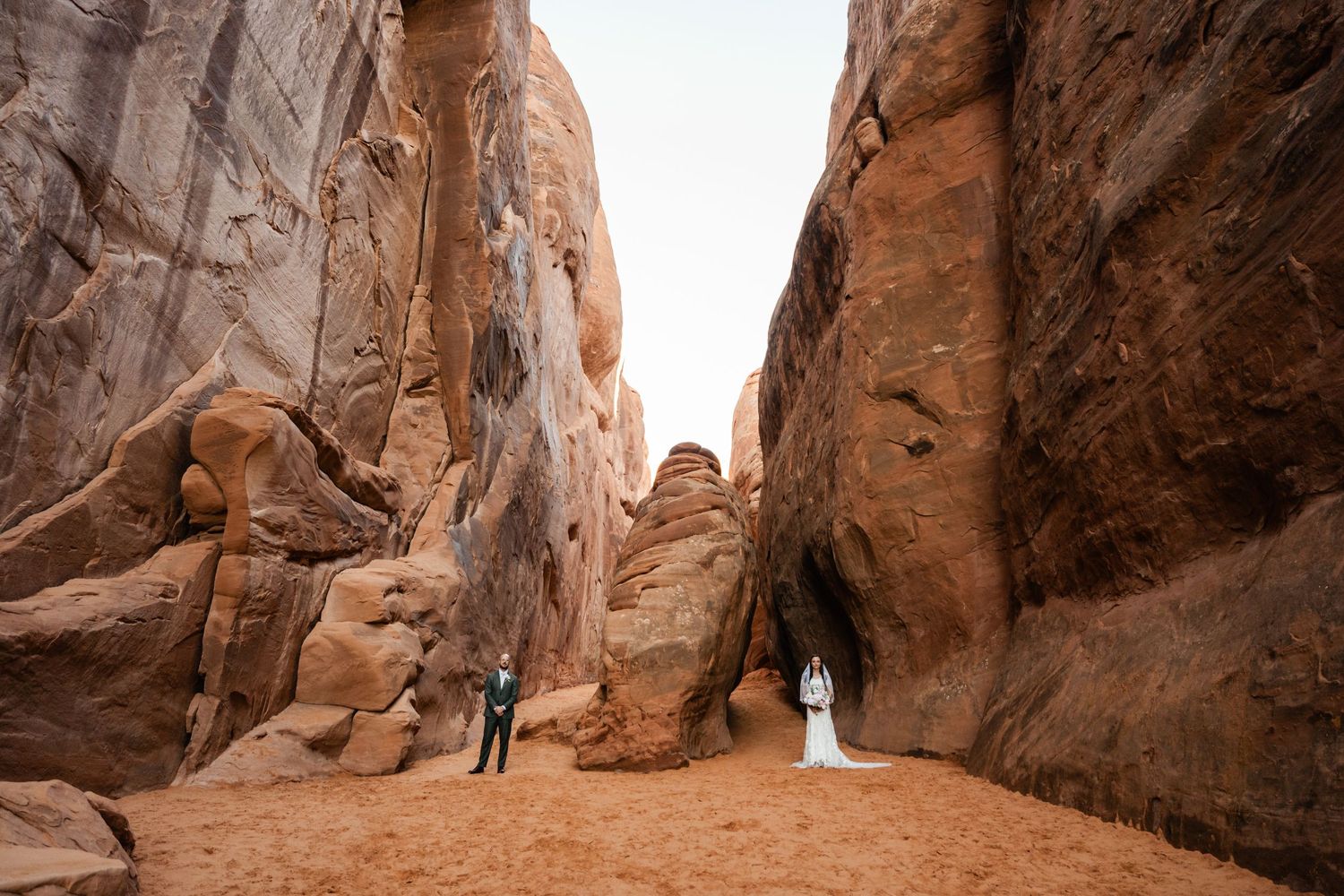 Towering red canyon walls create a natural corridor in a desert landscape.