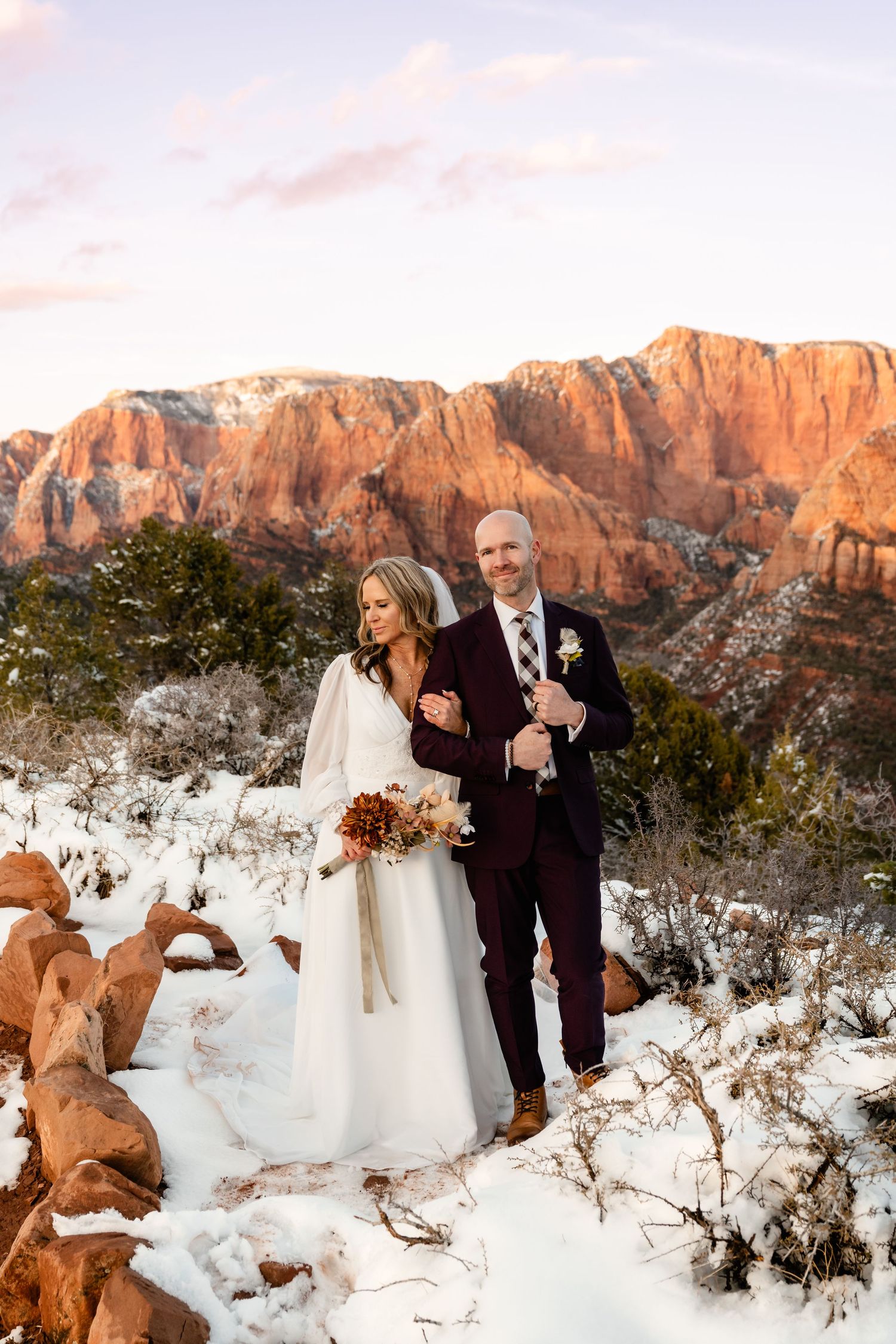 Winter wedding ceremony amidst snow-covered red rocks with golden sunset light on canyon walls.