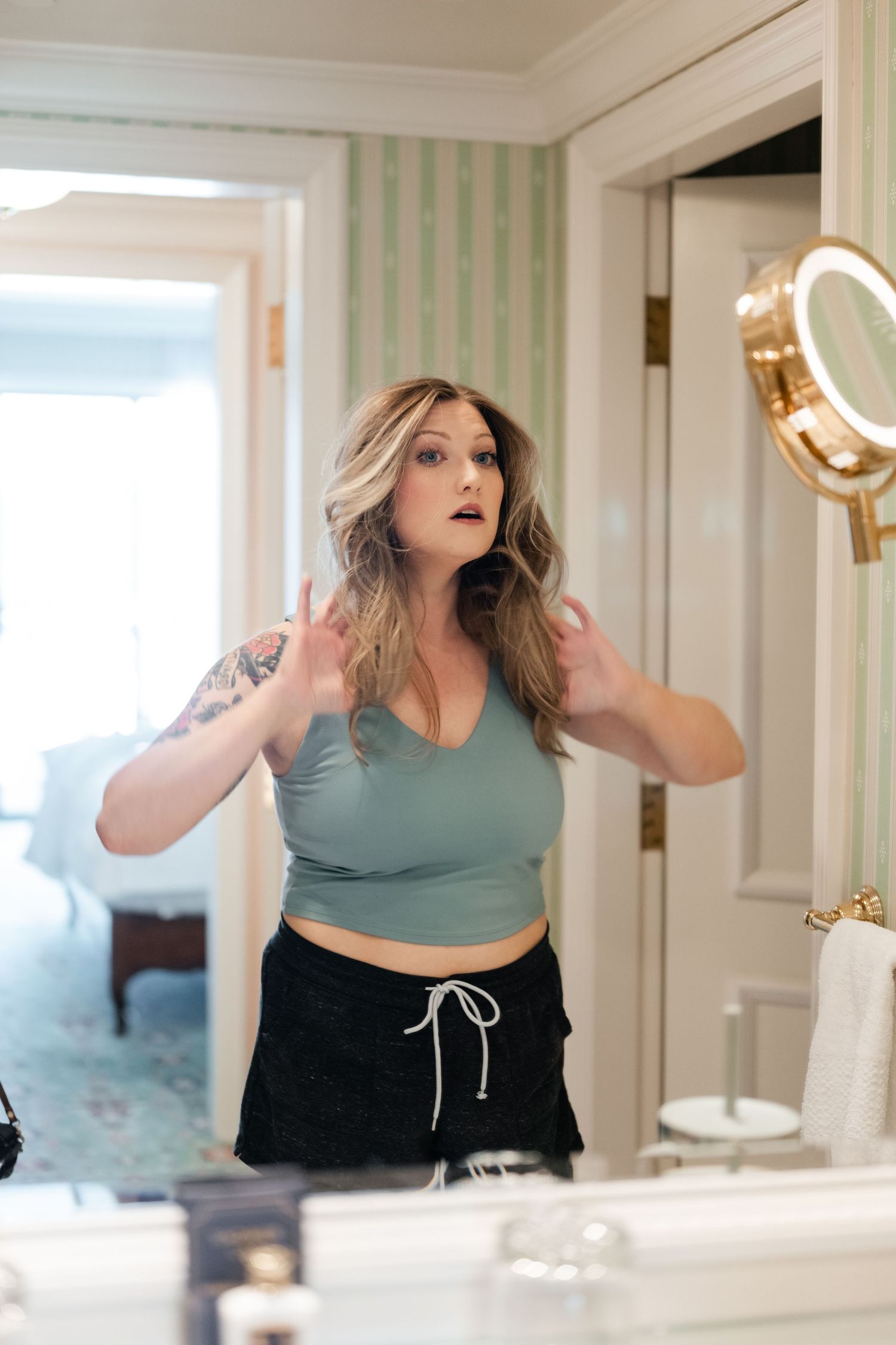 Person in teal sports bra and black pants strikes dramatic poses in front of bathroom mirror.