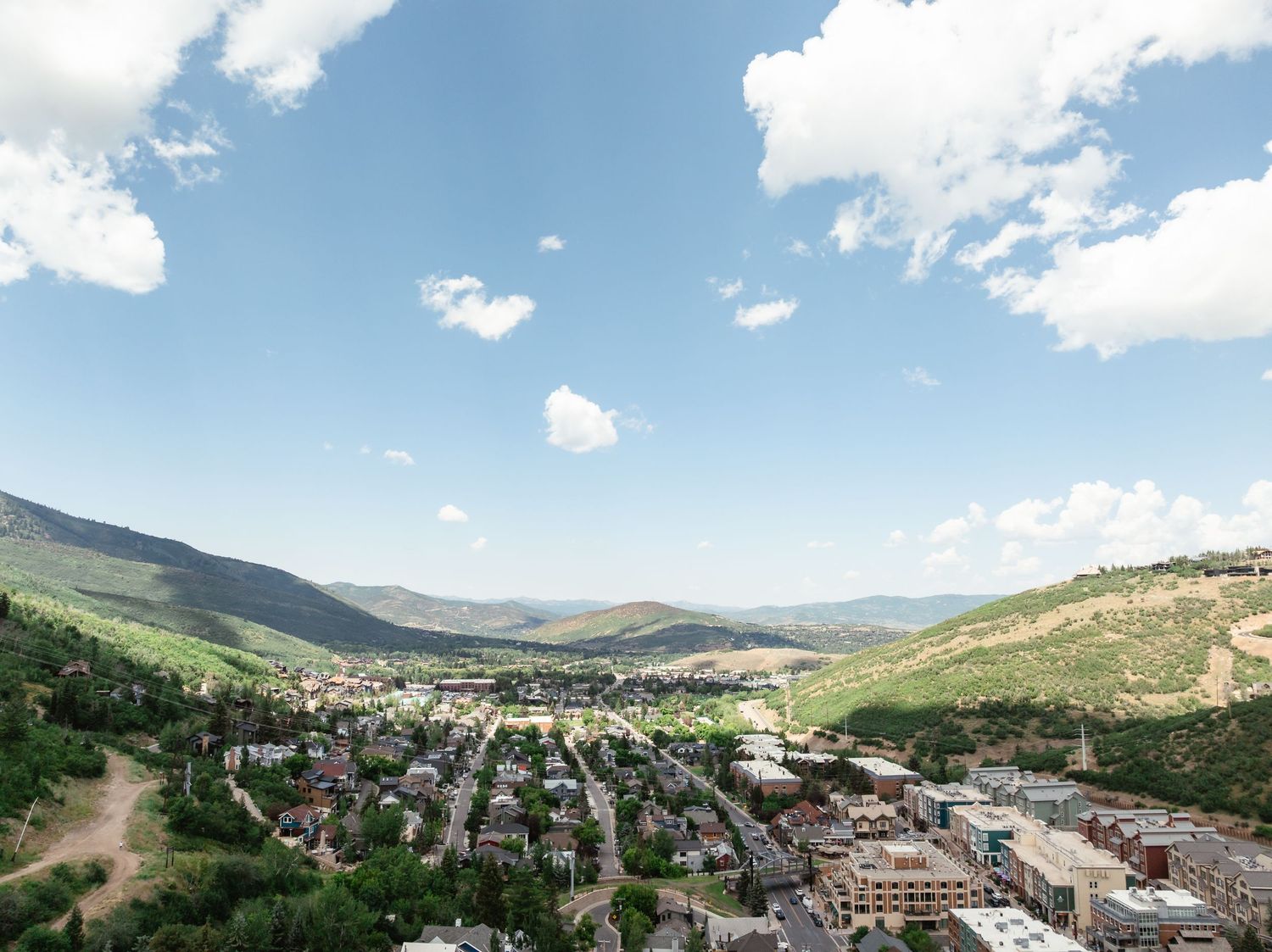 Panoramic mountain landscape view of a town nestled in a valley with rolling green hills and blue skies.