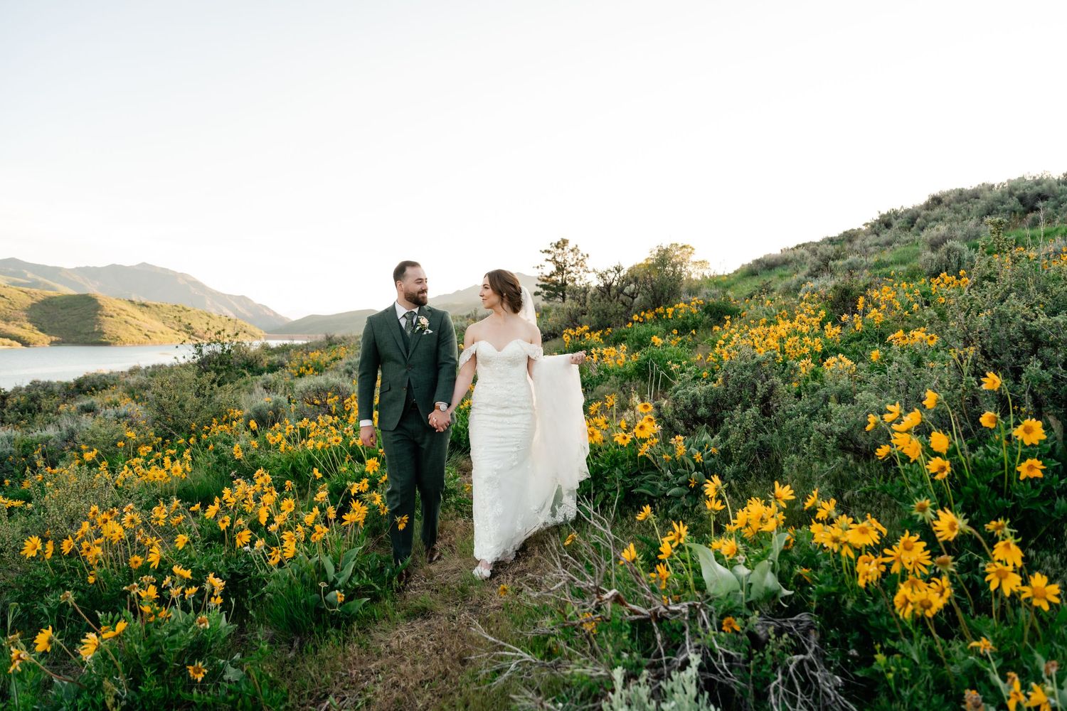 Couple walking through vibrant yellow wildflower fields on a hillside during golden hour.