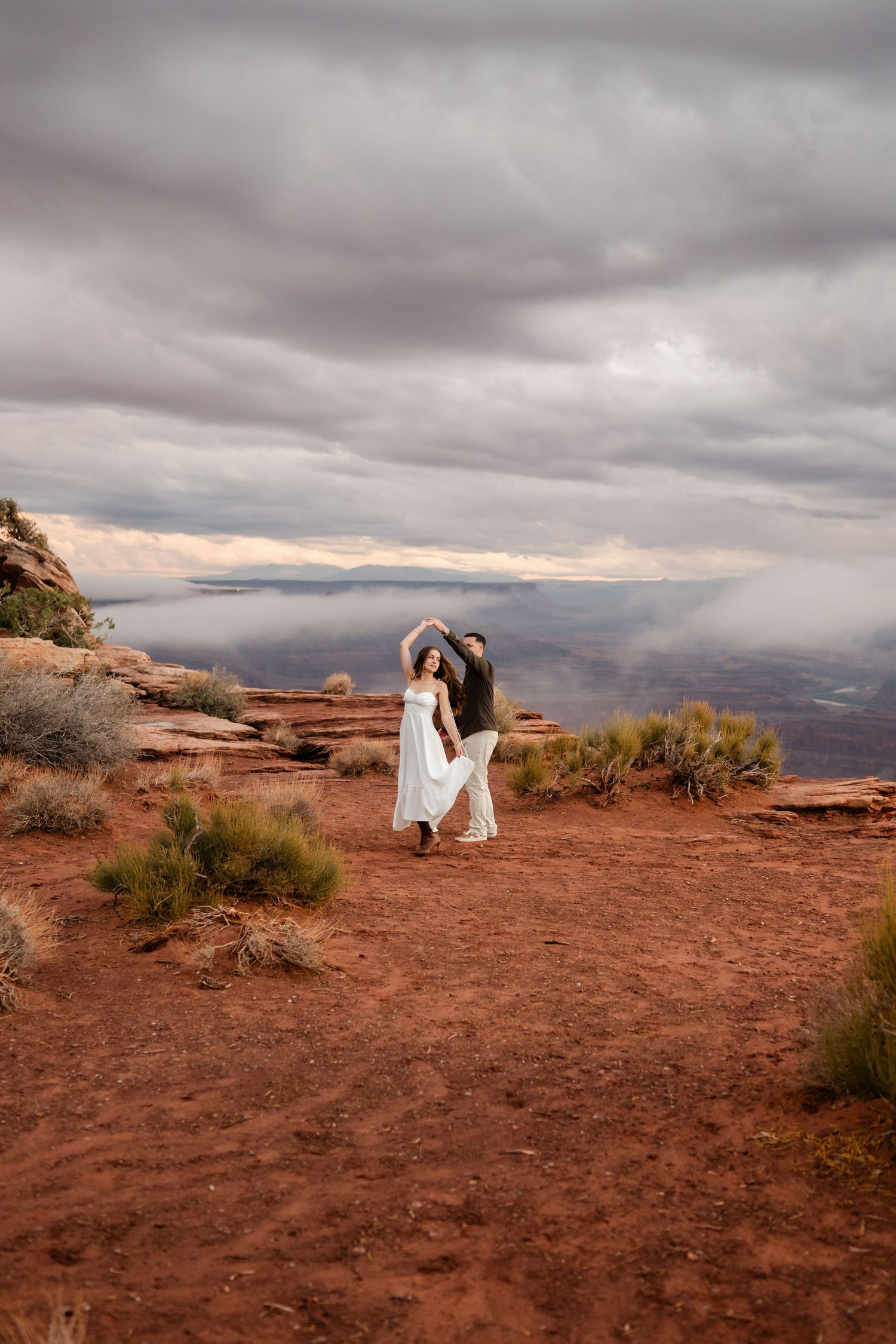 A romantic photoshoot on red desert rocks with dramatic stormy clouds at sunset.