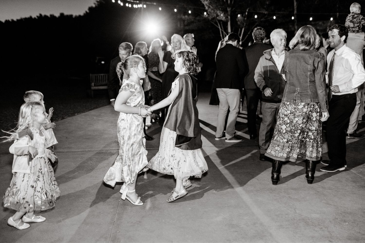 Wedding guests dance in formal attire during evening reception celebration.