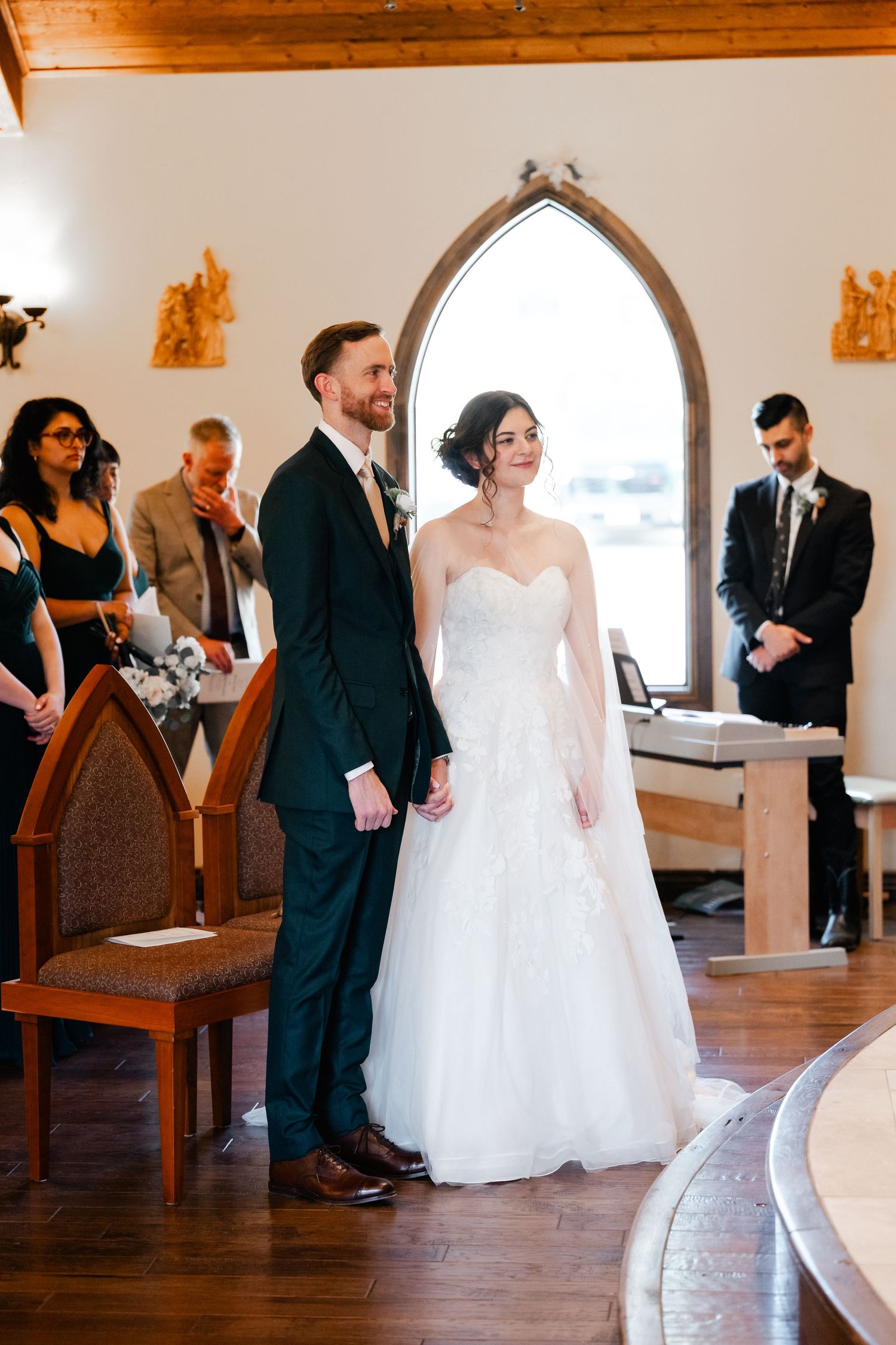 Wedding guests mingle in a bright church interior with arched windows and wooden pews.
