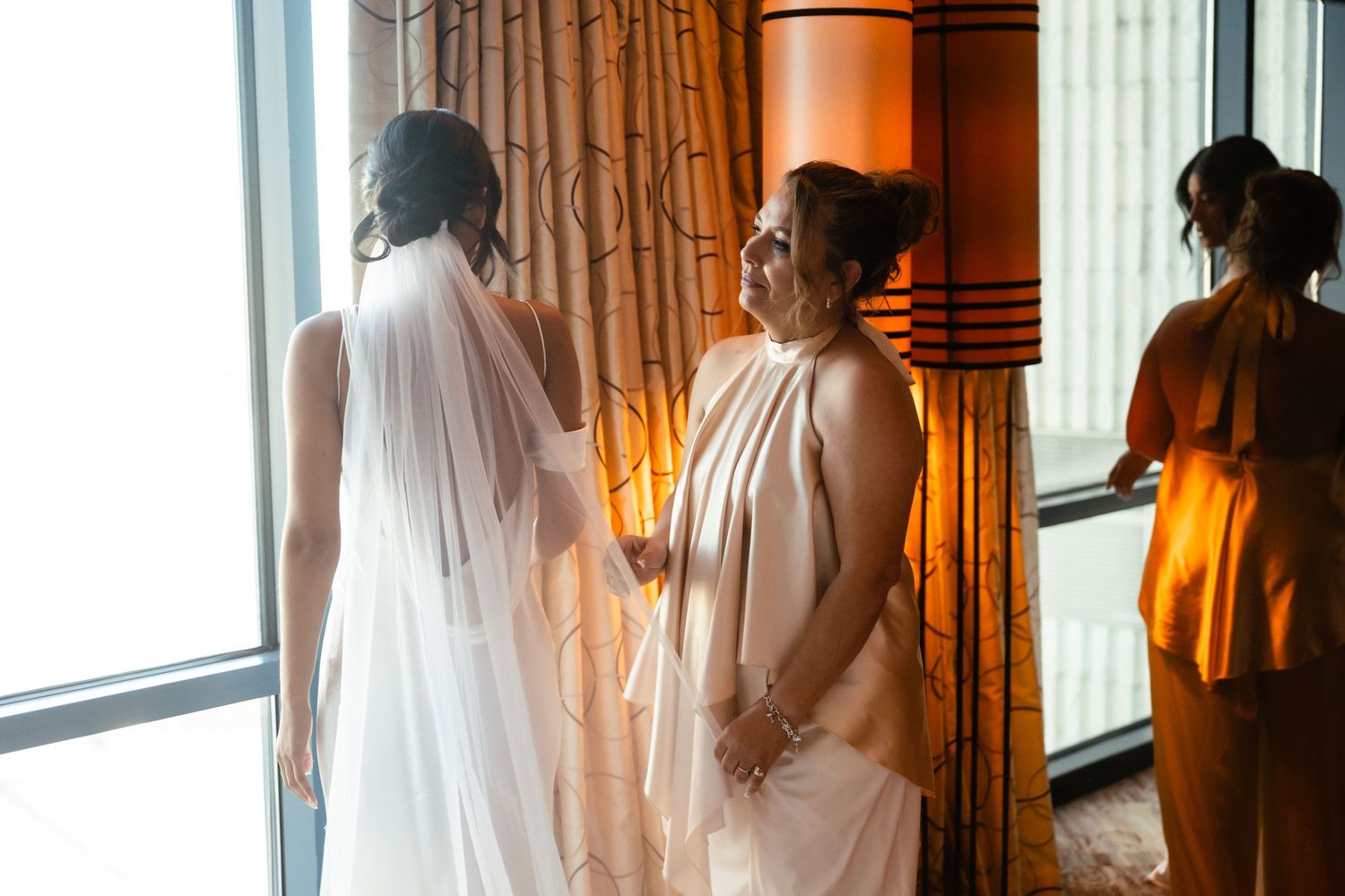 A series of silhouetted figures stand near windows in a warmly lit room with flowing curtains.