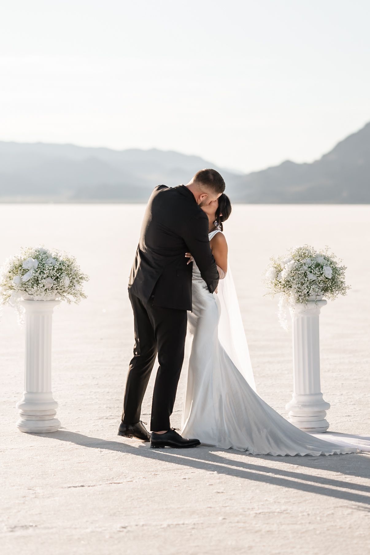 Romantic wedding portraits captured on a salt flat with decorative white pillars and floral arrangements.
