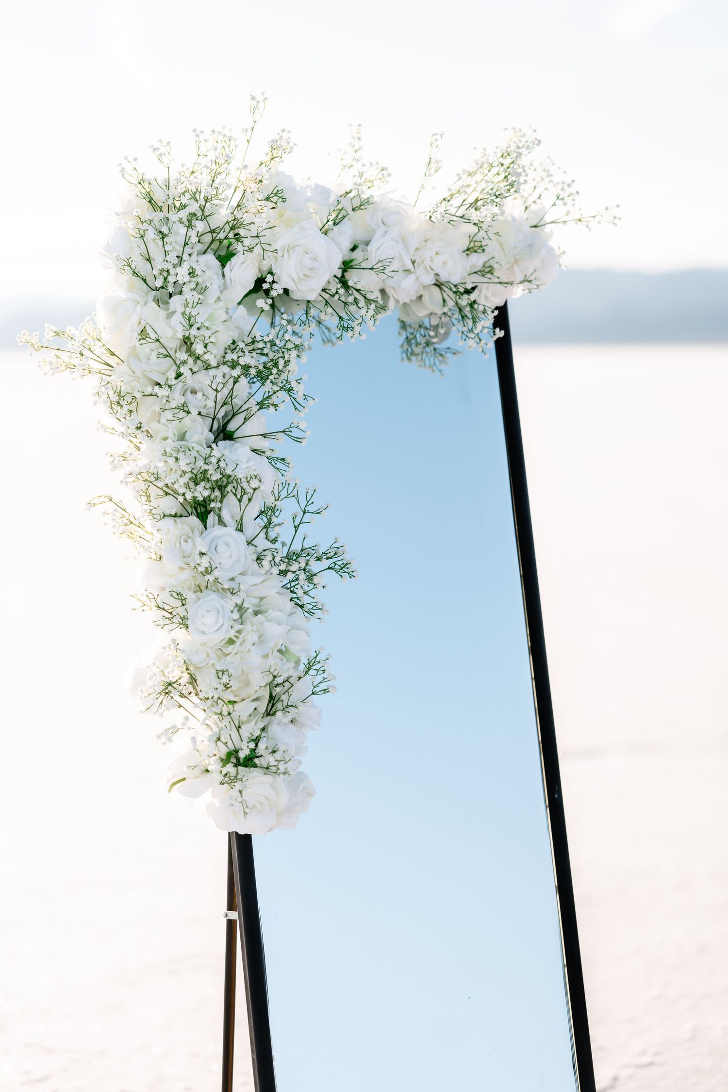 White floral arrangements on black stands against a light blue sky create an elegant outdoor ceremony setup.