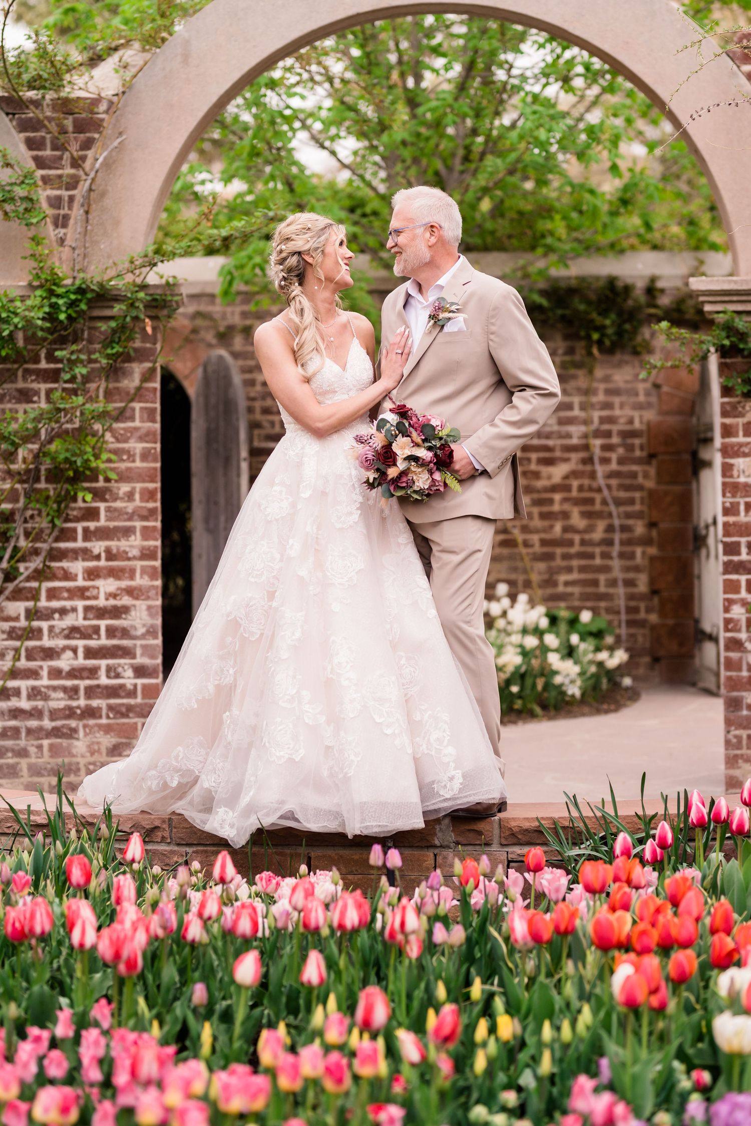 A couple dances together in a garden courtyard surrounded by blooming pink and red tulips under stone archways. Thanksgiving Point.
