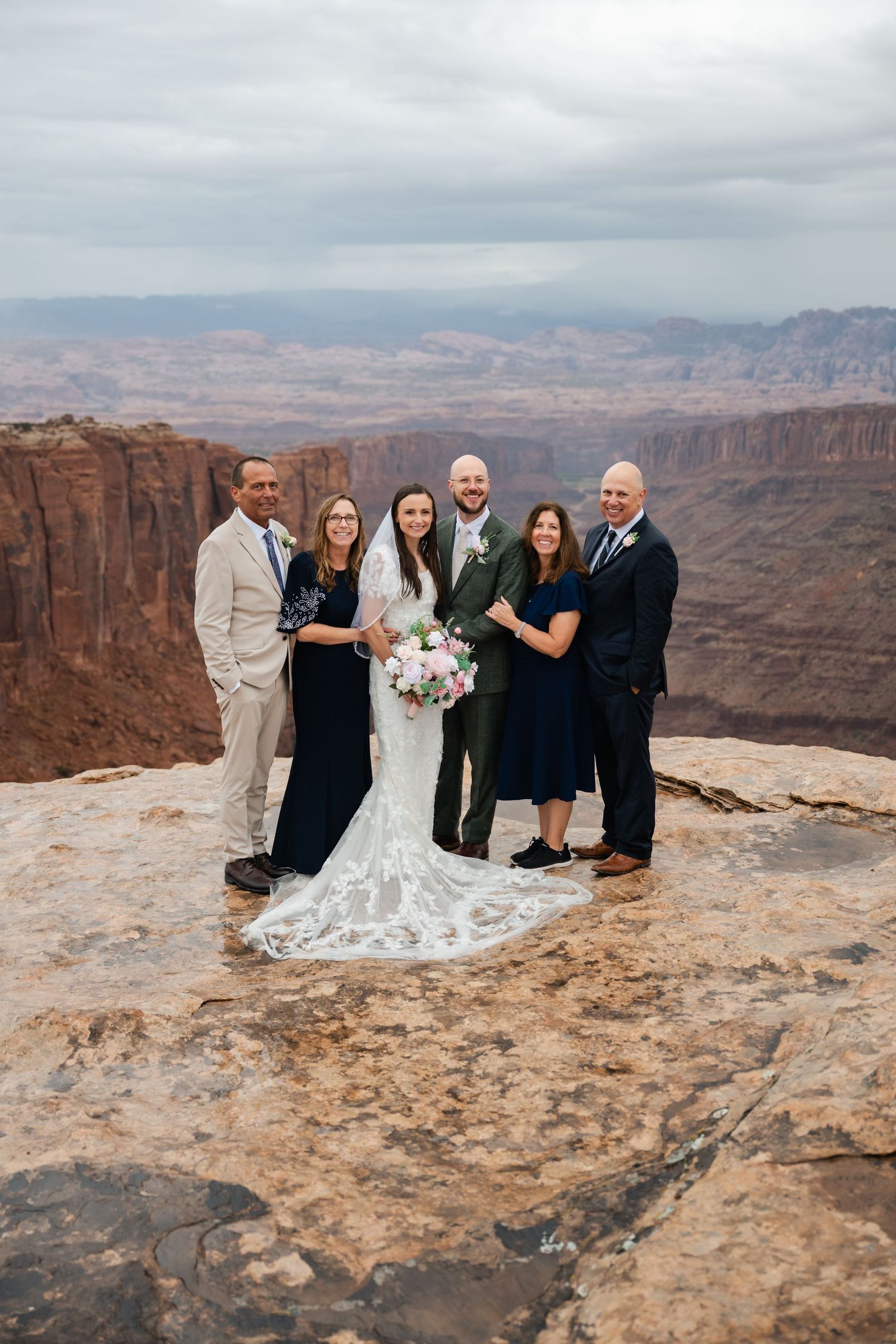 Wedding party gathers on scenic canyon overlook for group photos against dramatic desert landscape.