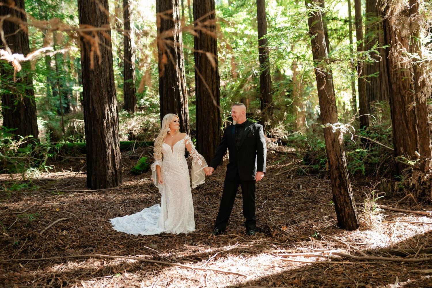 A wedding couple walking hand in hand through a majestic redwood forest.