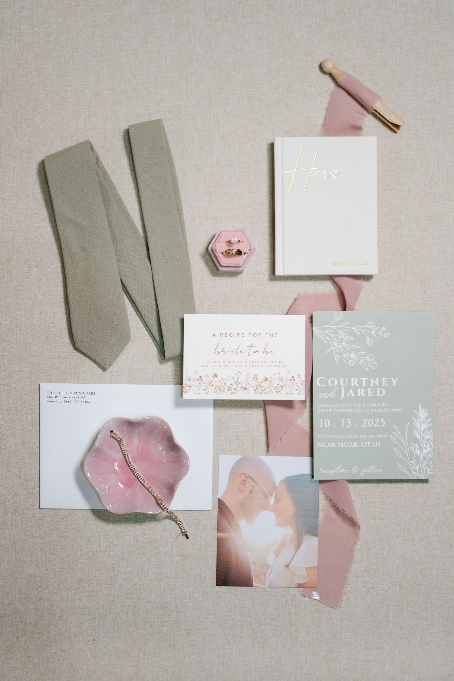 Wedding stationery flatlay featuring sage green and blush pink colors with elegant invitations and ribbons.