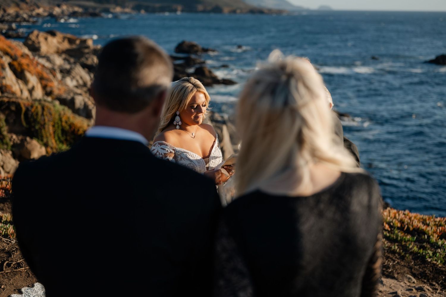 Blurred silhouettes of wedding attendees against a dramatic ocean backdrop.
