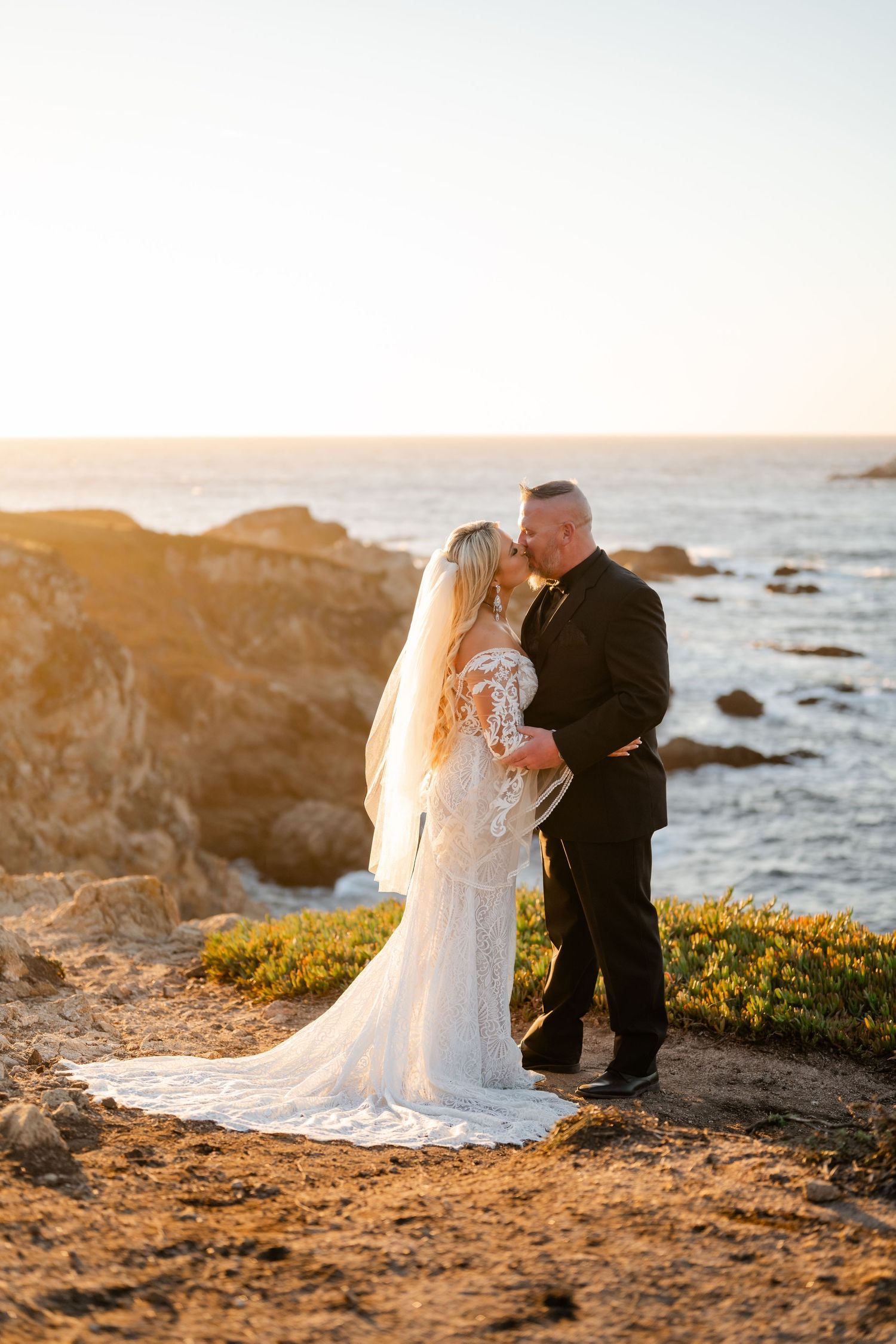 A tender moment between newlyweds on a coastal cliff during golden hour.